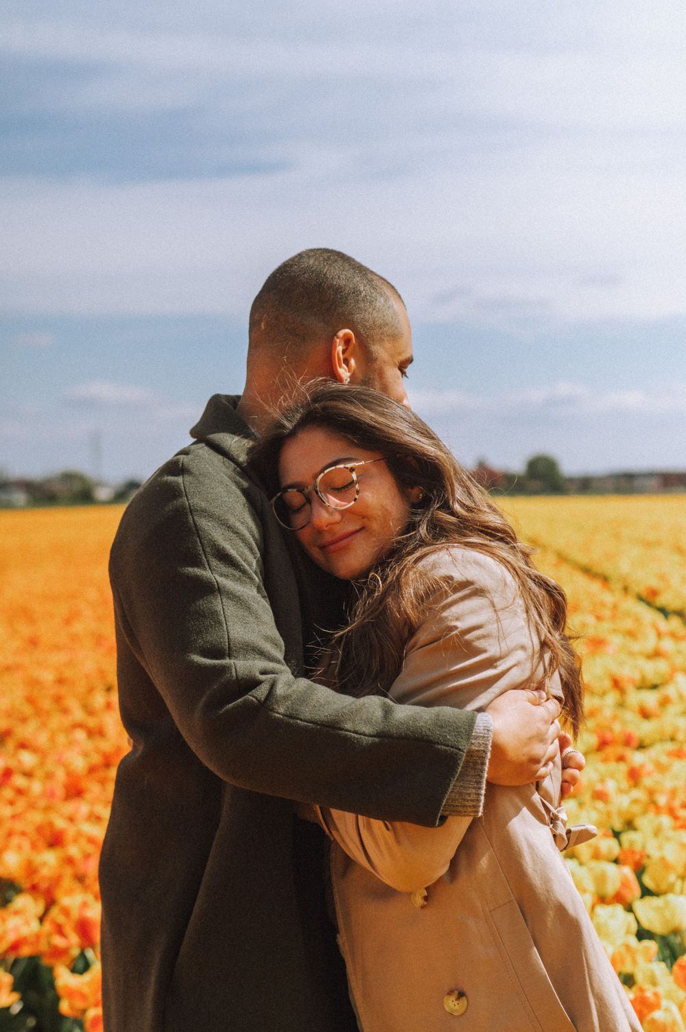 Romantic couple embracing in a vibrant orange tulip field during sunset.