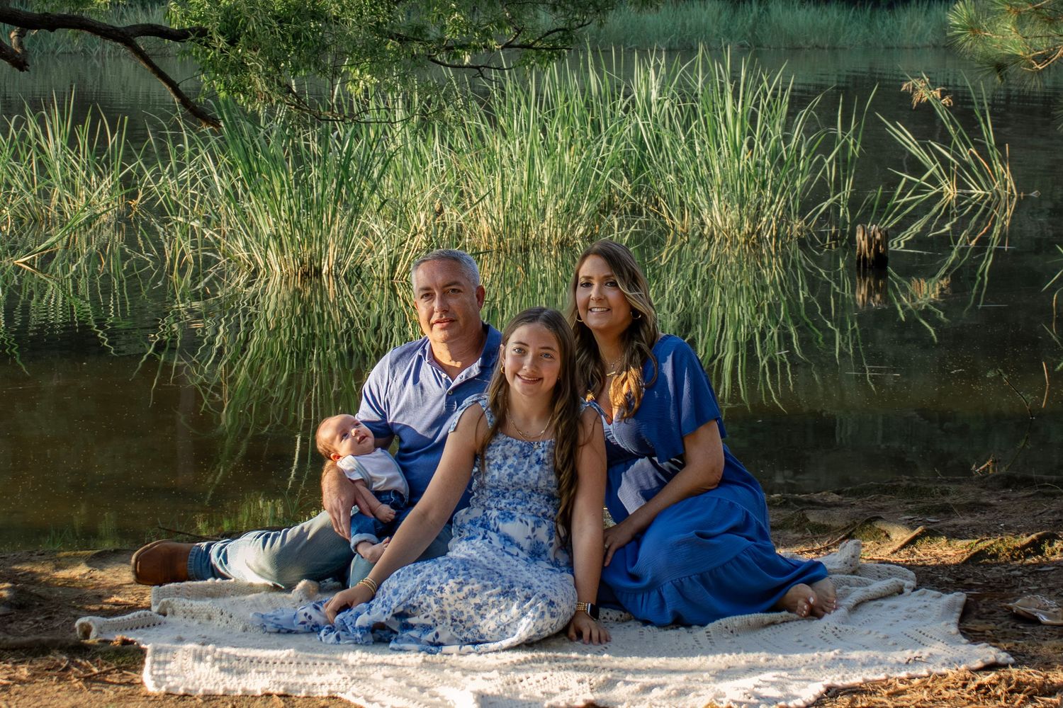Three people and a small dog sitting on a blanket by a pond with tall reeds in the background Lake Wateree SC. Captured by Raley and Roots.