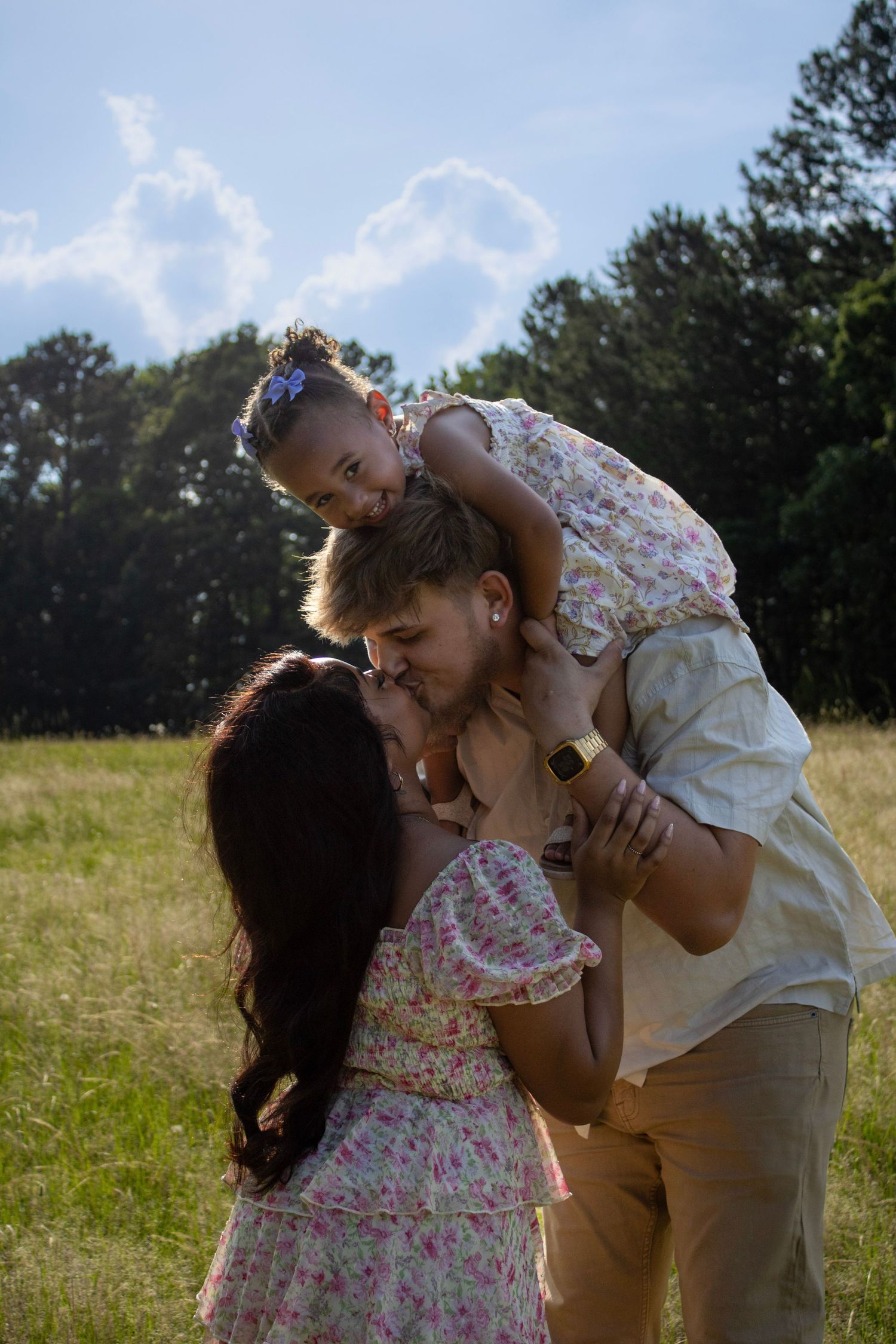 A family shares a tender moment together in a sunlit meadow on a bright summer day in Ridgeway, South Carolina, captured by Raley and Roots.