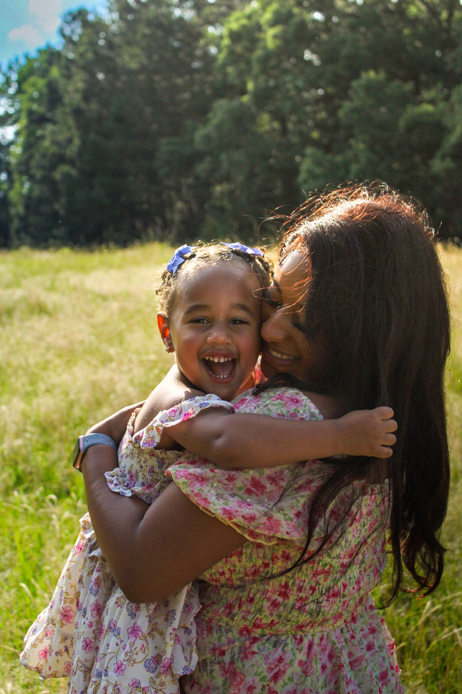 A loving moment captured in nature as mother and daughter embrace and smile joyfully in a sunny meadow during SC Family Photo Session.