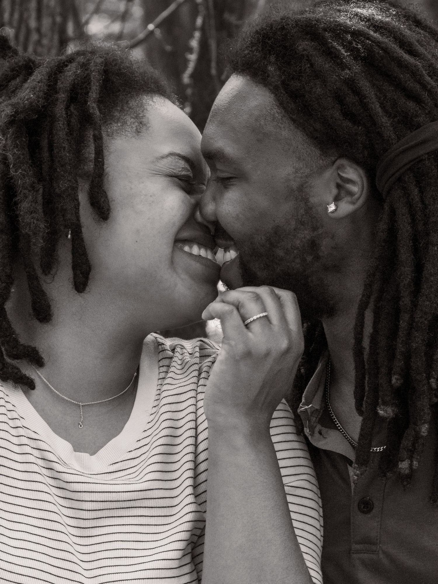 A couple with dreadlocks shares an intimate moment while smiling and holding hands.