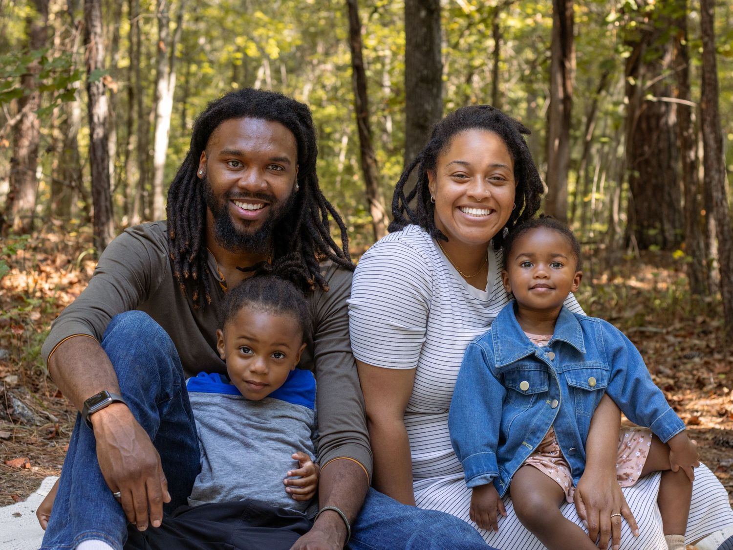 A happy family of four poses together for a portrait in an autumn forest.