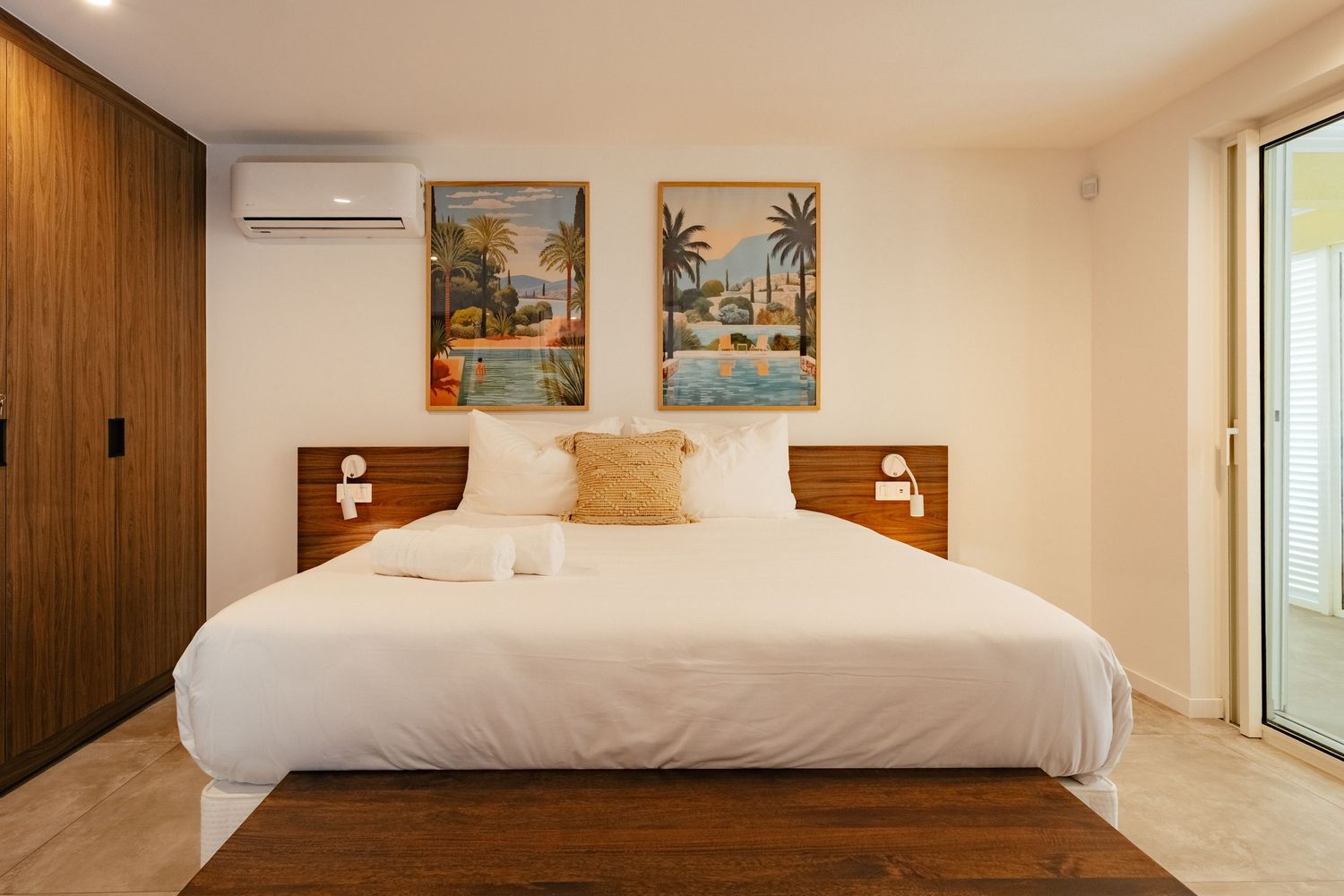 Contemporary hotel bedroom with coastal artwork, white bedding, and wooden accents.