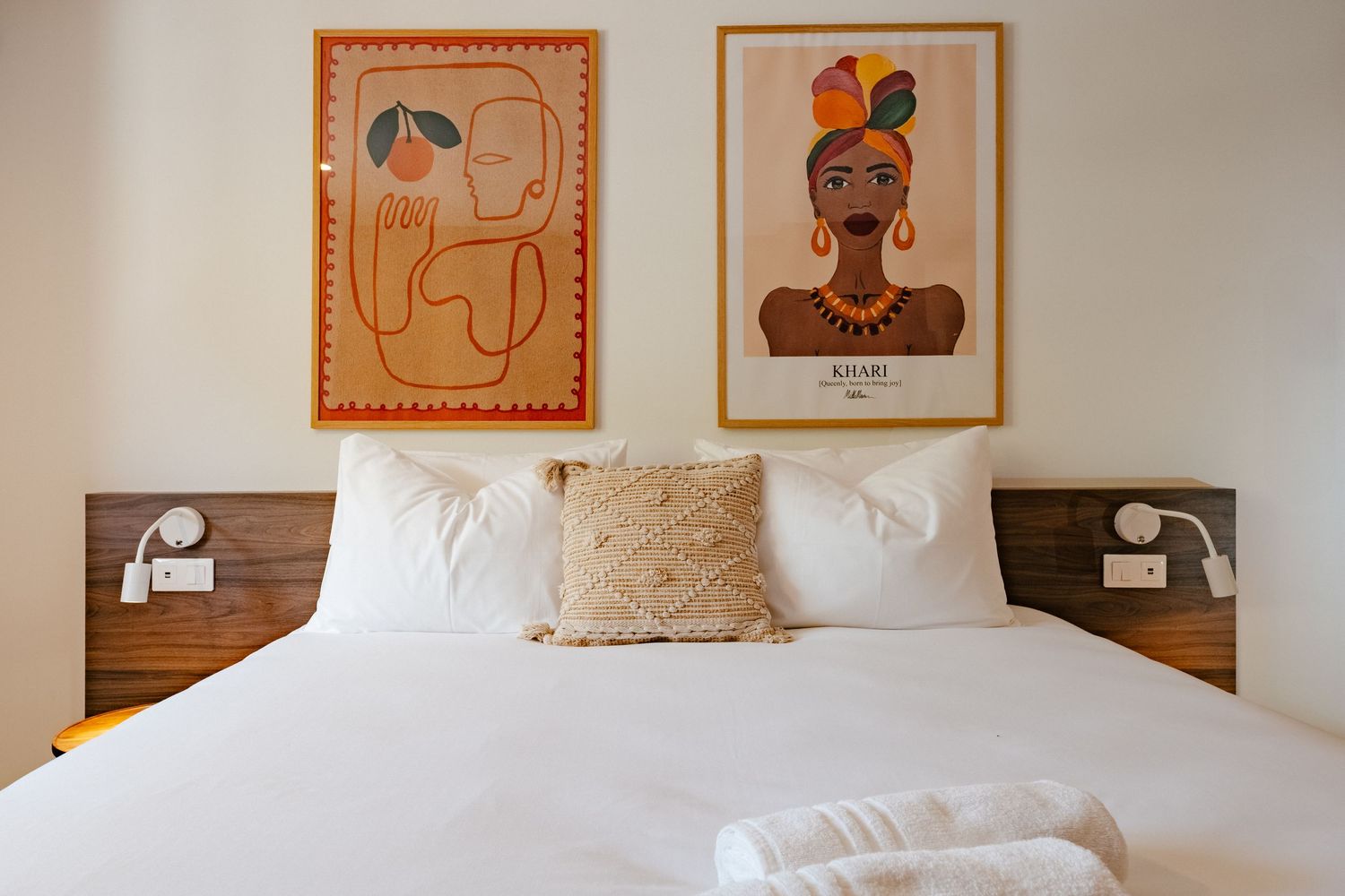 Modern bedroom featuring abstract art prints above white bedding and wooden headboard.