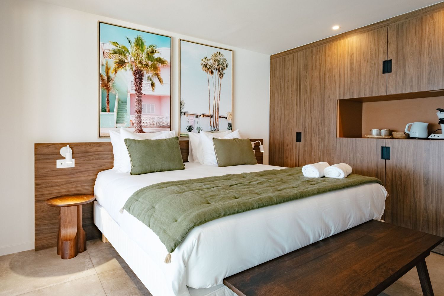 Modern hotel room interior with wood paneling, king bed with green accent pillows, and floor-to-ceiling windows.