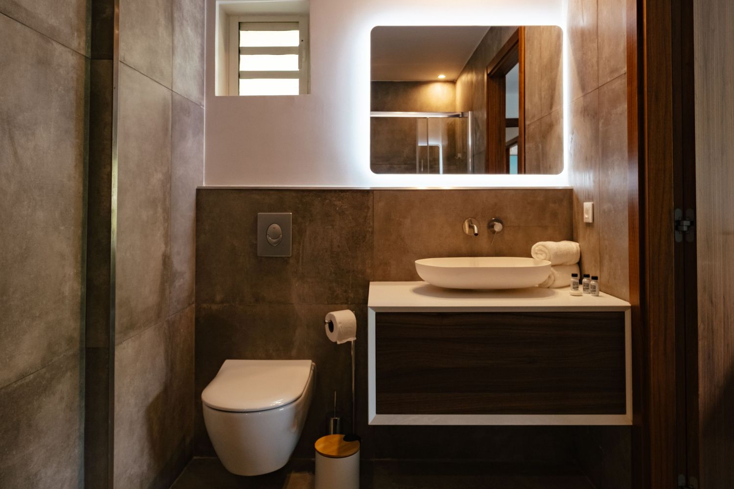 Modern minimalist bathroom interior with floating vanity, wall-mounted toilet, and natural stone tiled walls.