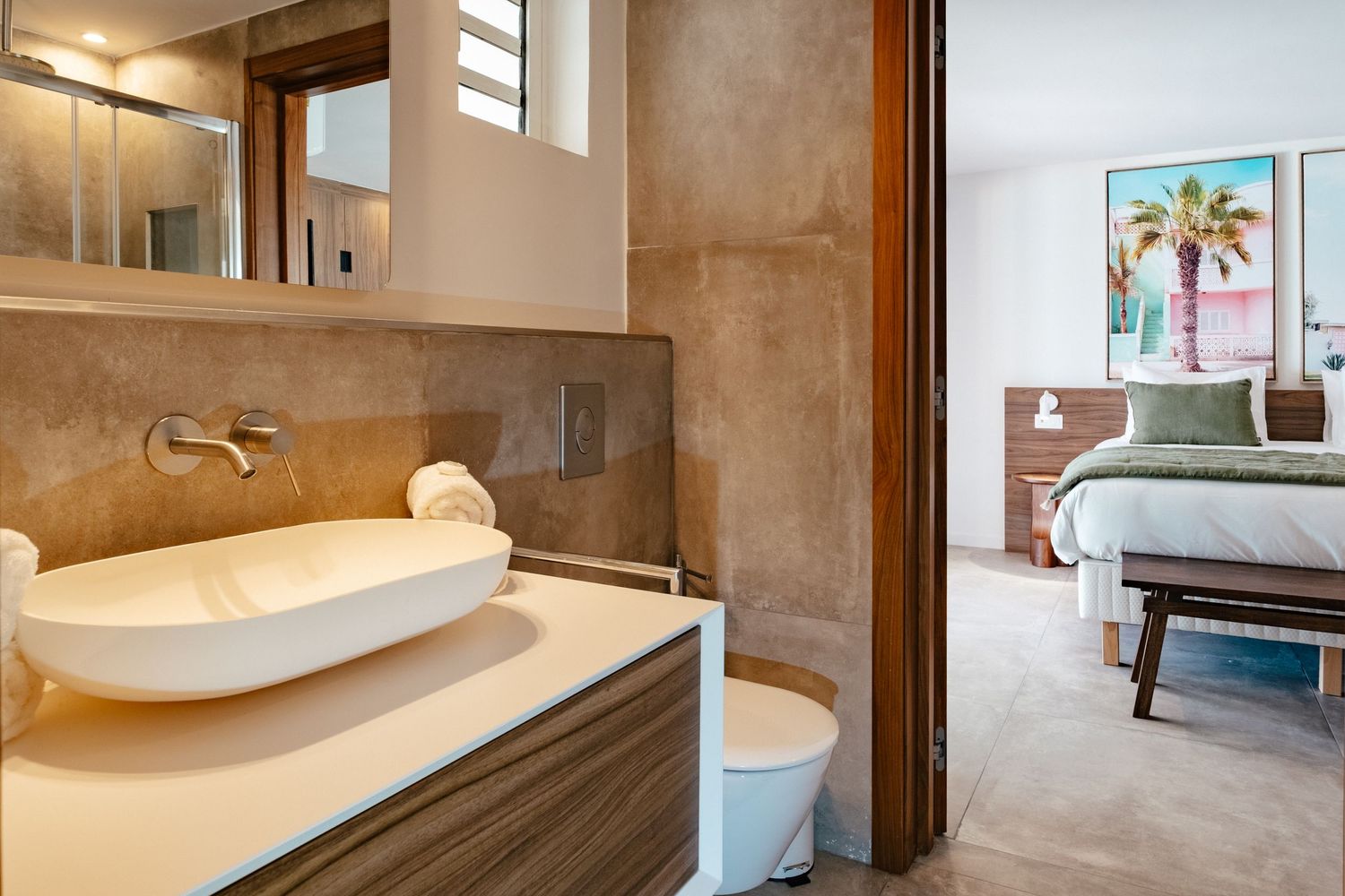 Modern bathroom with vessel sink and warm wood tones connecting to a tropical-themed bedroom suite.