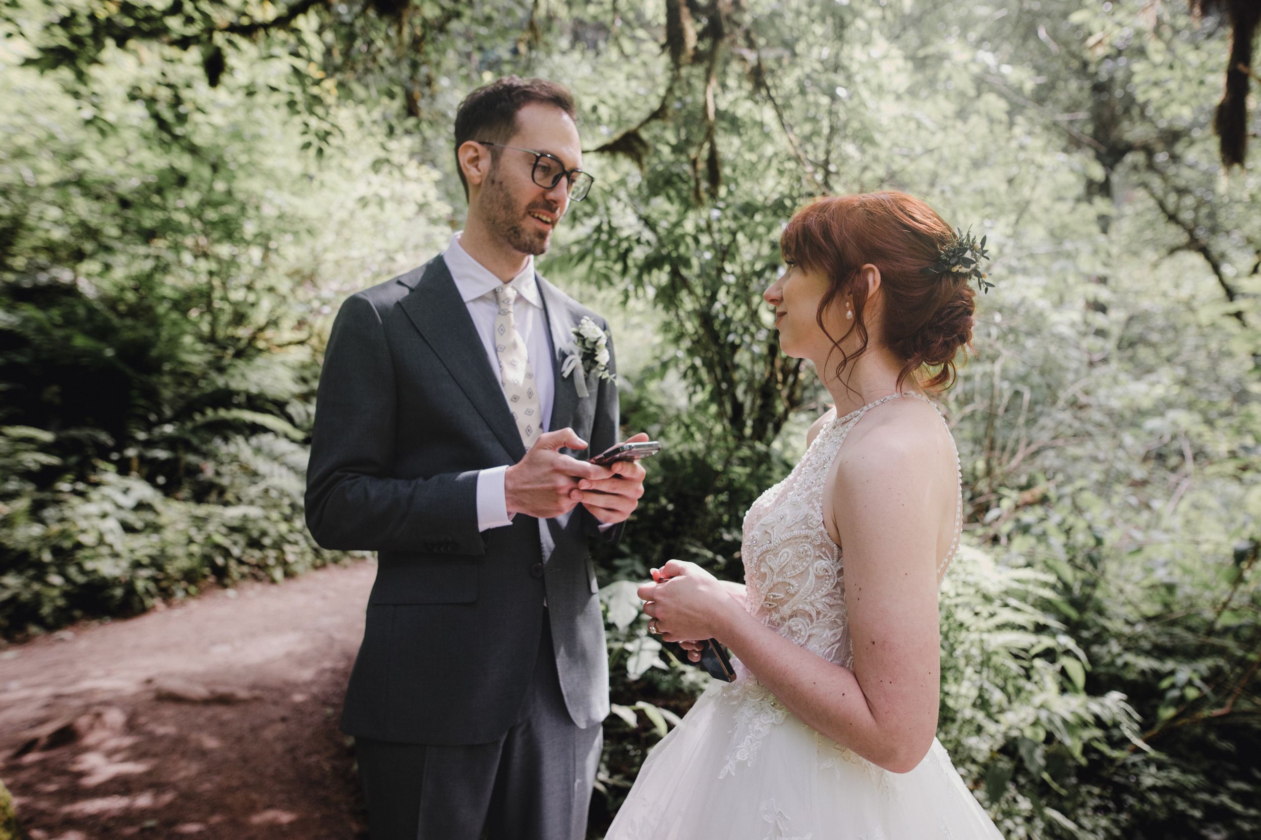 A couple shares a tender moment in a lush forest setting wearing formal wedding attire.