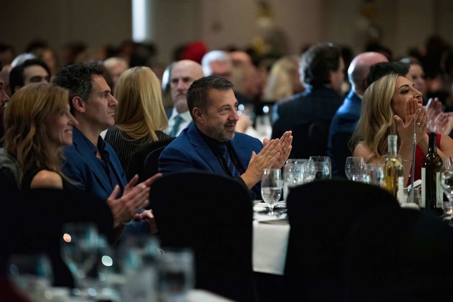 Guests seated at dinner tables clapping during Kelowna Business Excellence Awards gala - Okanagan event photography by Tania Veitch.