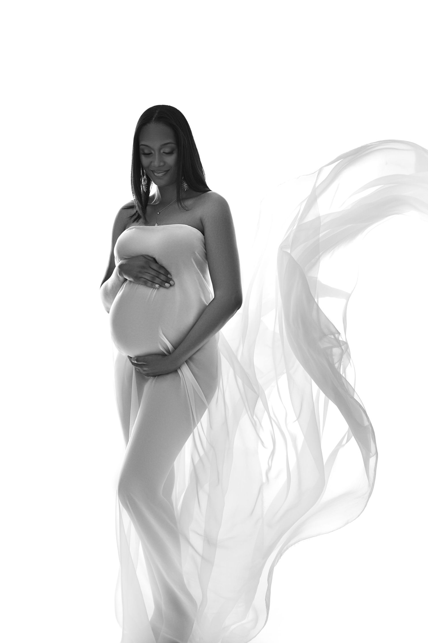 A series of elegant black and white maternity portraits showing a silhouette draped in flowing white fabric.