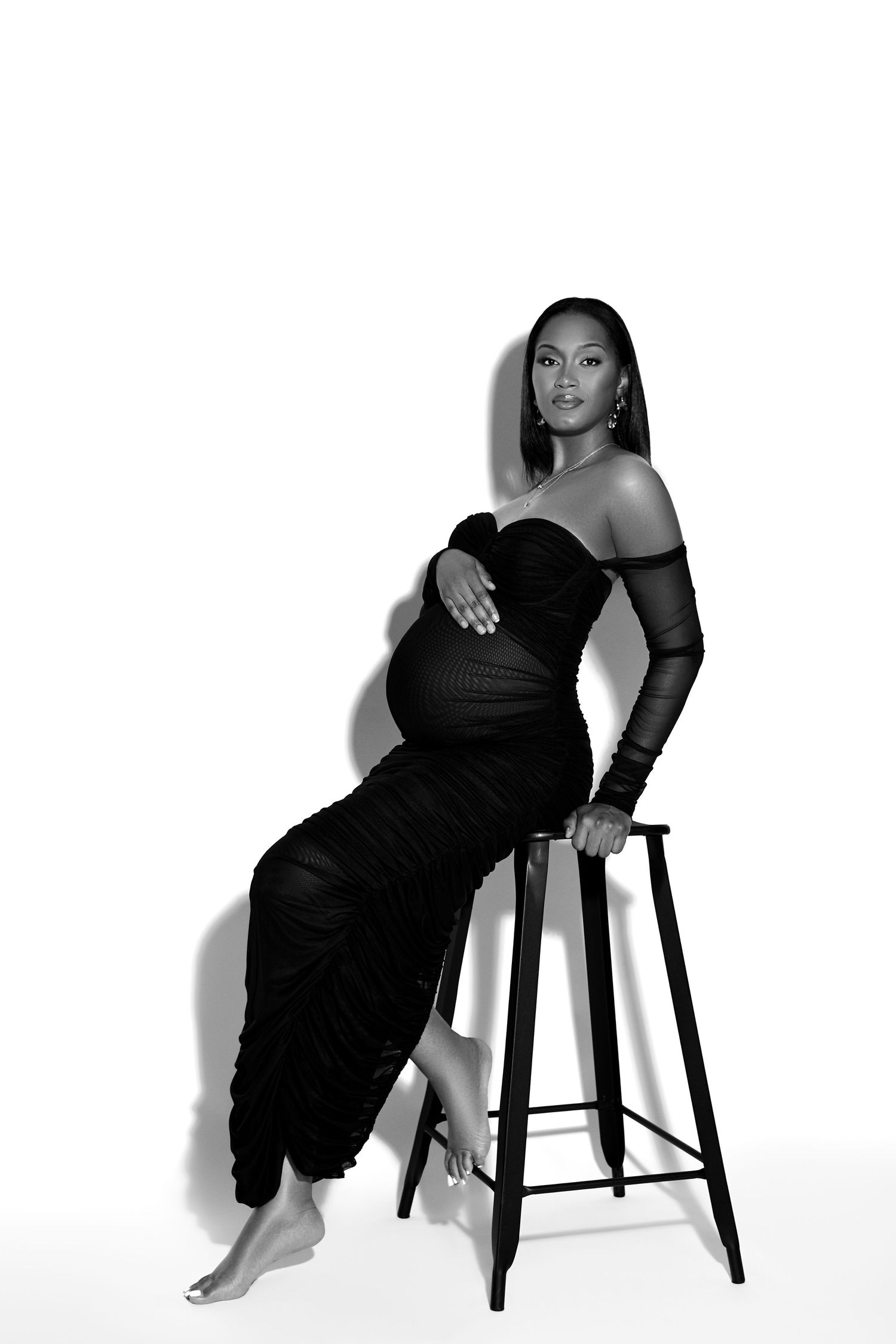Artistic black and white portrait series showing person in black dress posing elegantly on bar stool against white backdrop.
