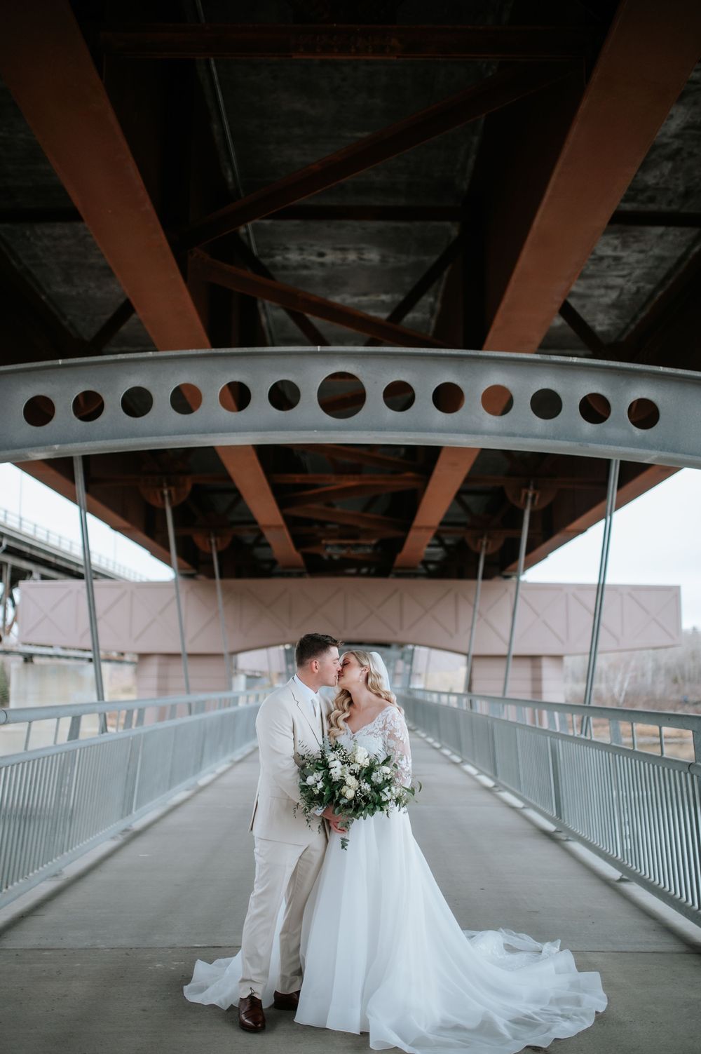 Romantic wedding couple embracing on a covered bridge walkway with industrial architectural details.