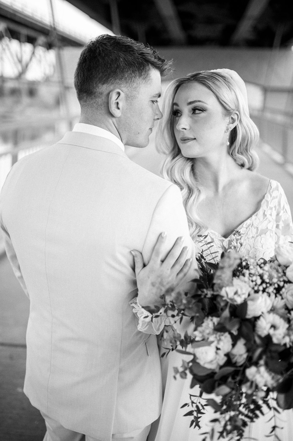 A romantic black and white wedding photo of a couple with a bouquet of flowers on a covered walkway.