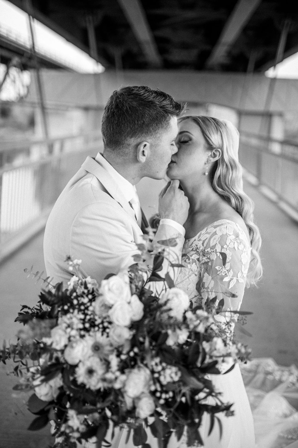 A romantic black and white wedding photo showing a couple sharing a tender moment with a beautiful floral bouquet.