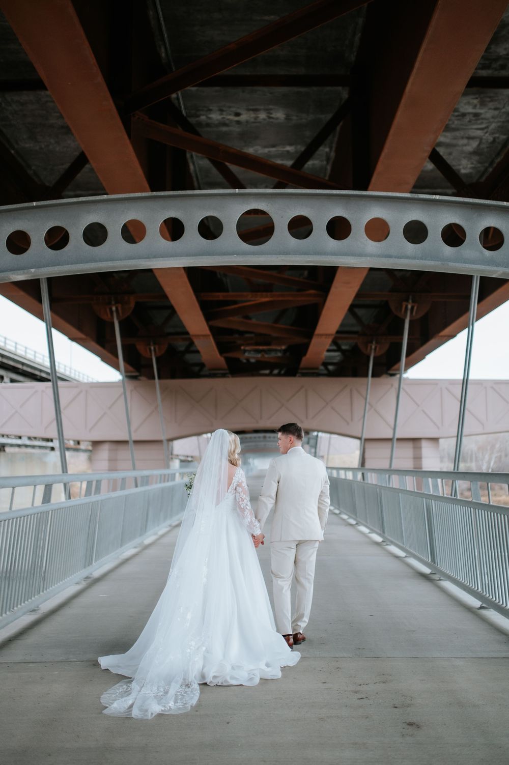 A couple in wedding attire stands in a covered bridge walkway from different perspectives in a photo series.