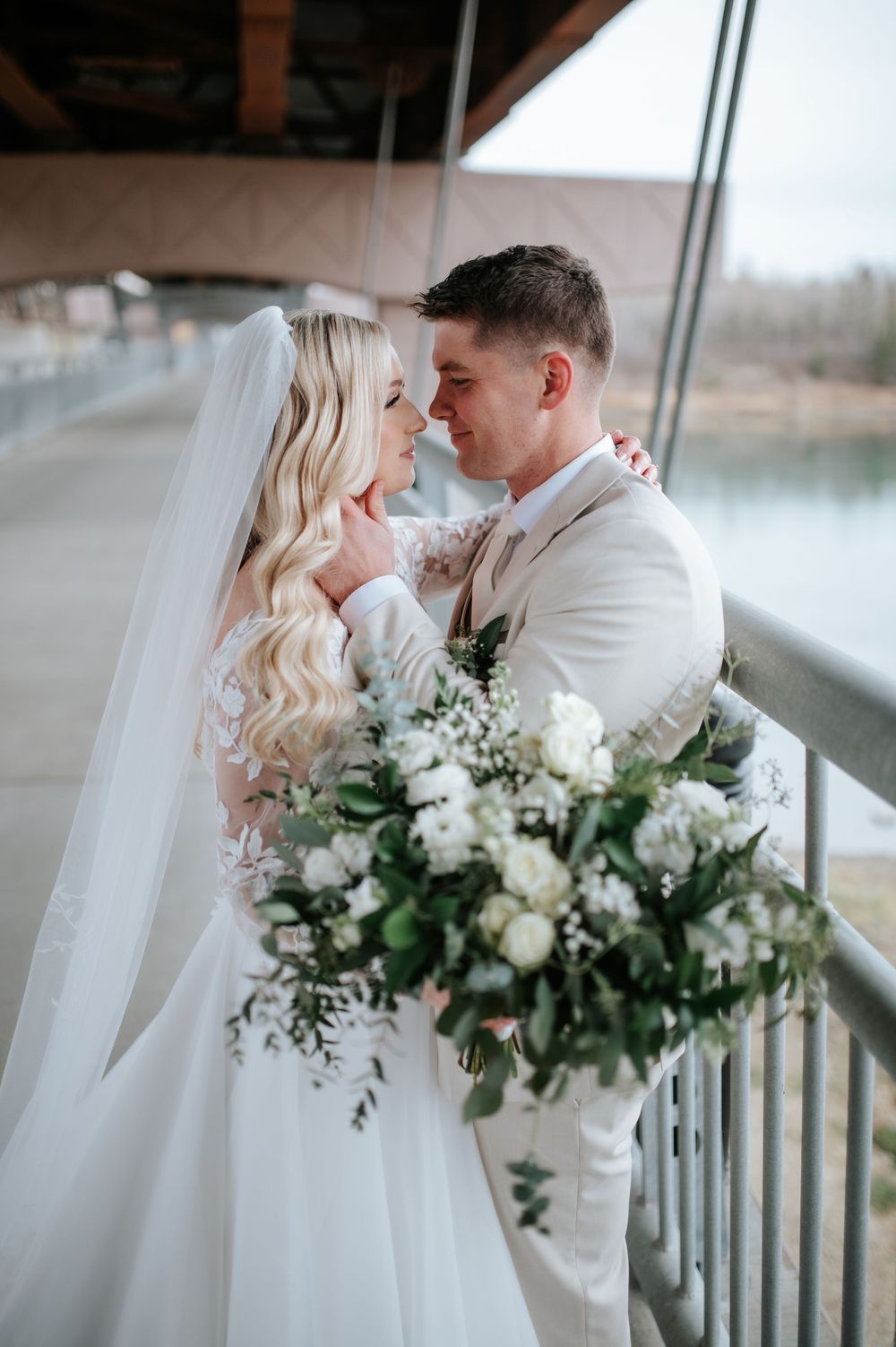 Romantic wedding couple shares intimate moments on a balcony with white florals and flowing veil in winter setting.