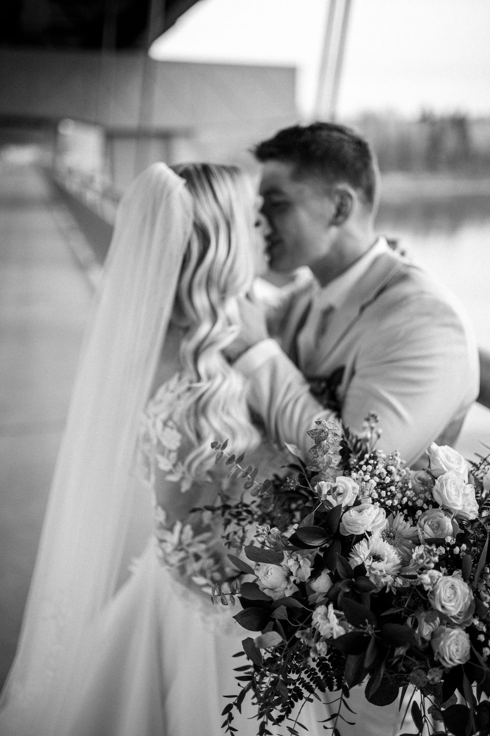 Intimate black and white wedding portrait with elegant floral bouquet featuring roses and greenery.