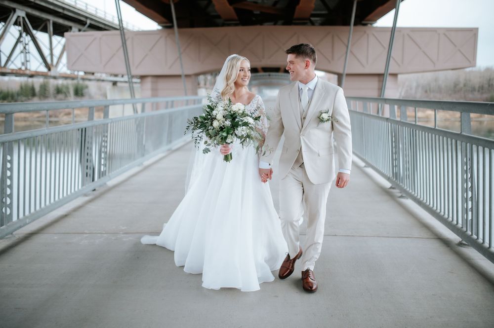 A couple on their wedding day walks together on a covered bridge wearing a white gown and light beige suit.