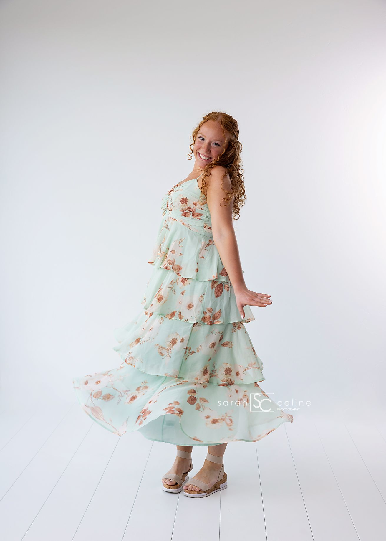 Figure in flowing mint green floral tiered maxi dress with ruffles twirls against white background.