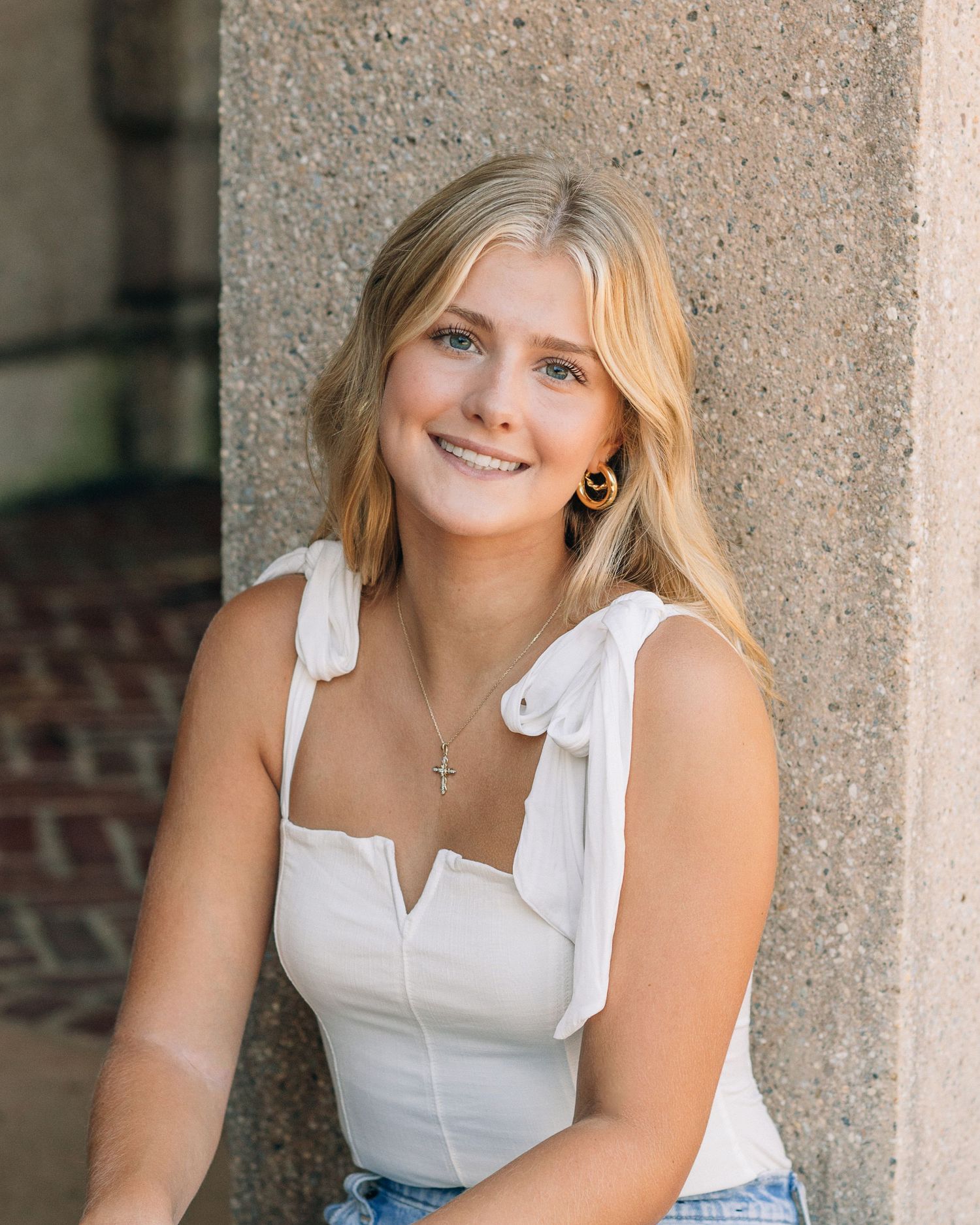 Portrait showing white summer top with bow straps against stone architectural backdrop.