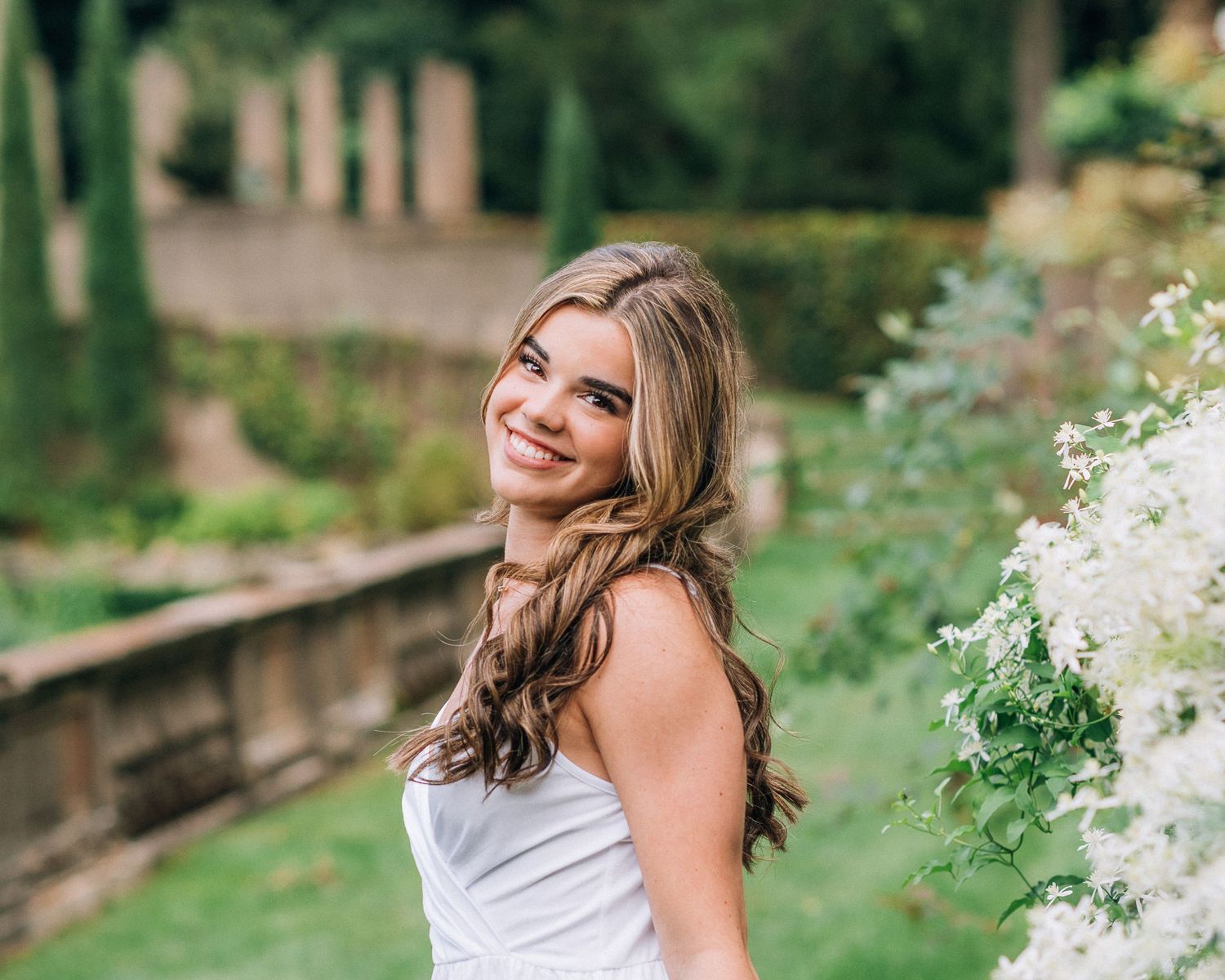 Summer portrait in white dress near blooming garden flowers.
