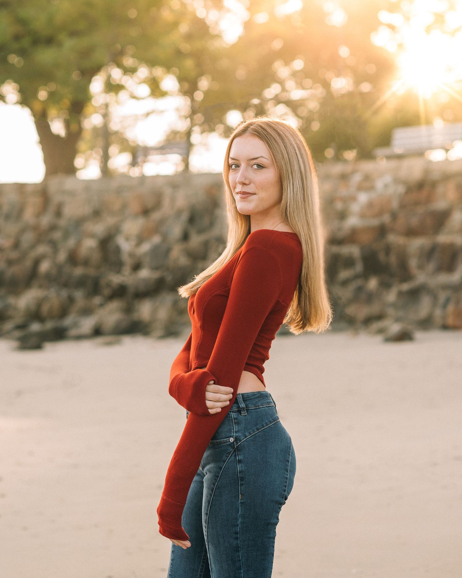 Portrait of woman in red sweater posing against stone wall during golden hour.