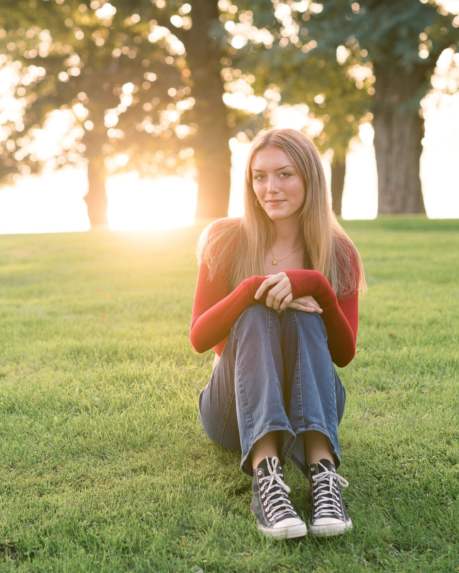 Casual outdoor portrait on grass with sun flare through trees.