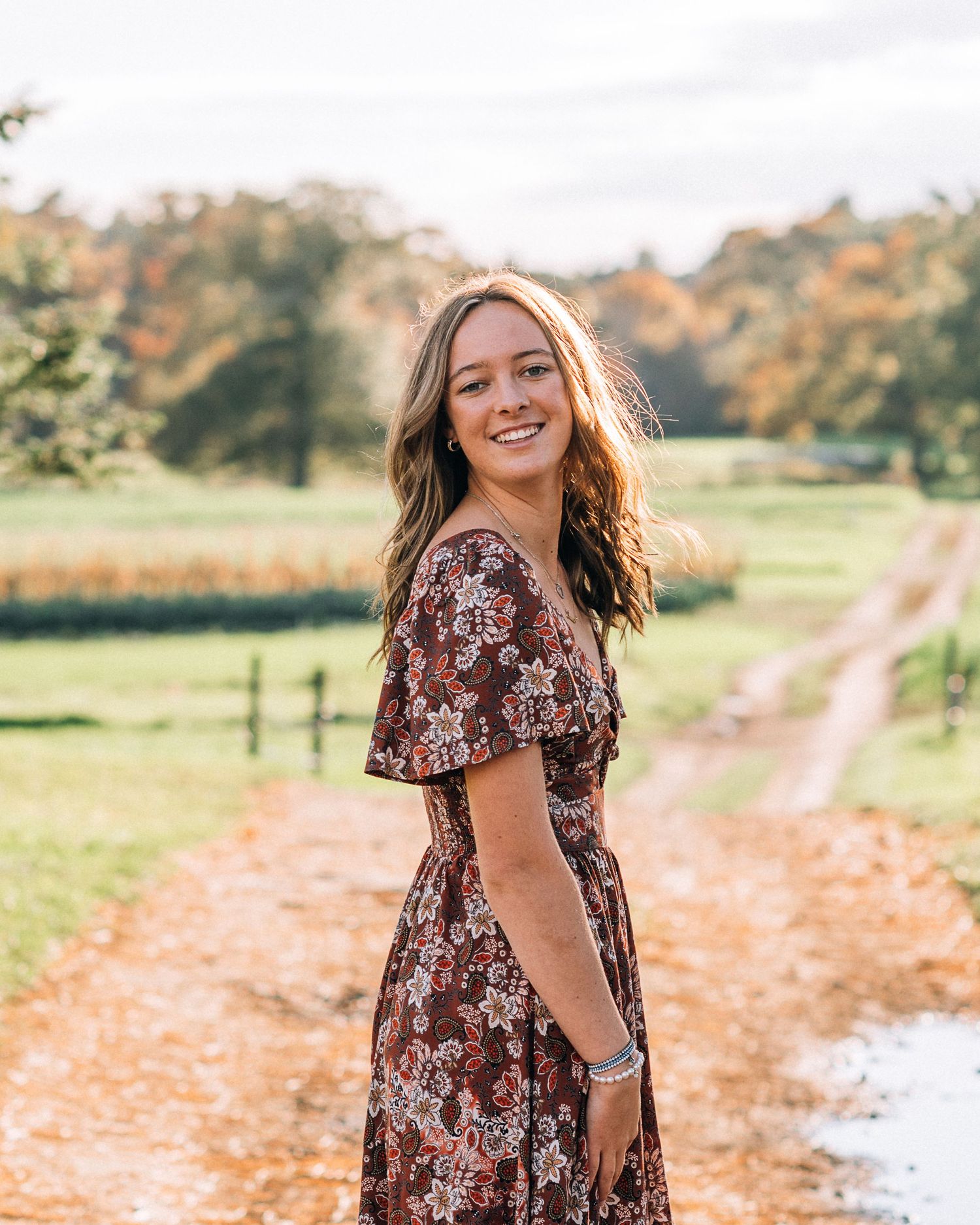 Autumn portrait in floral dress on dirt path with fall colors in background.