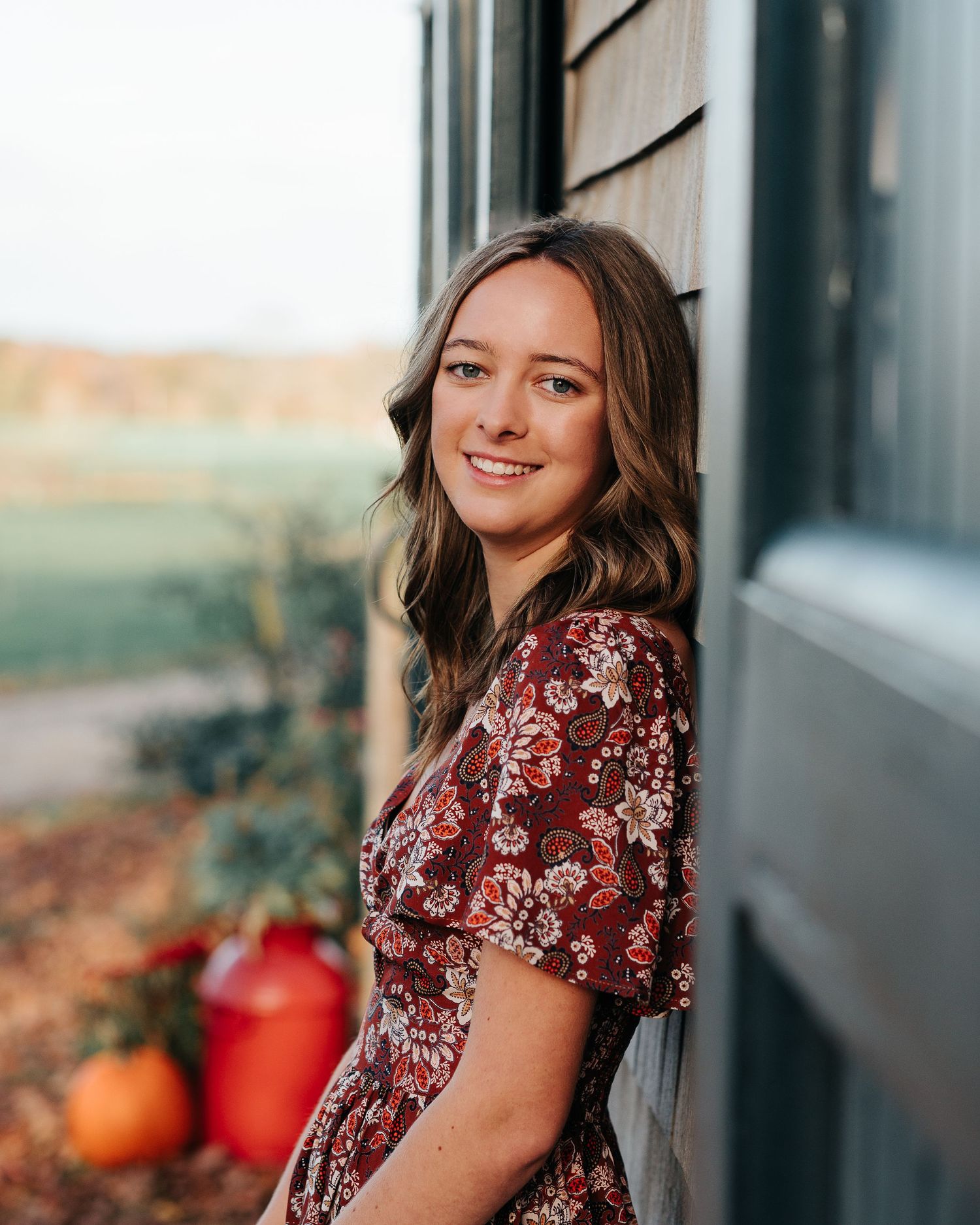 Portrait in burgundy floral dress next to house with fall decorations.