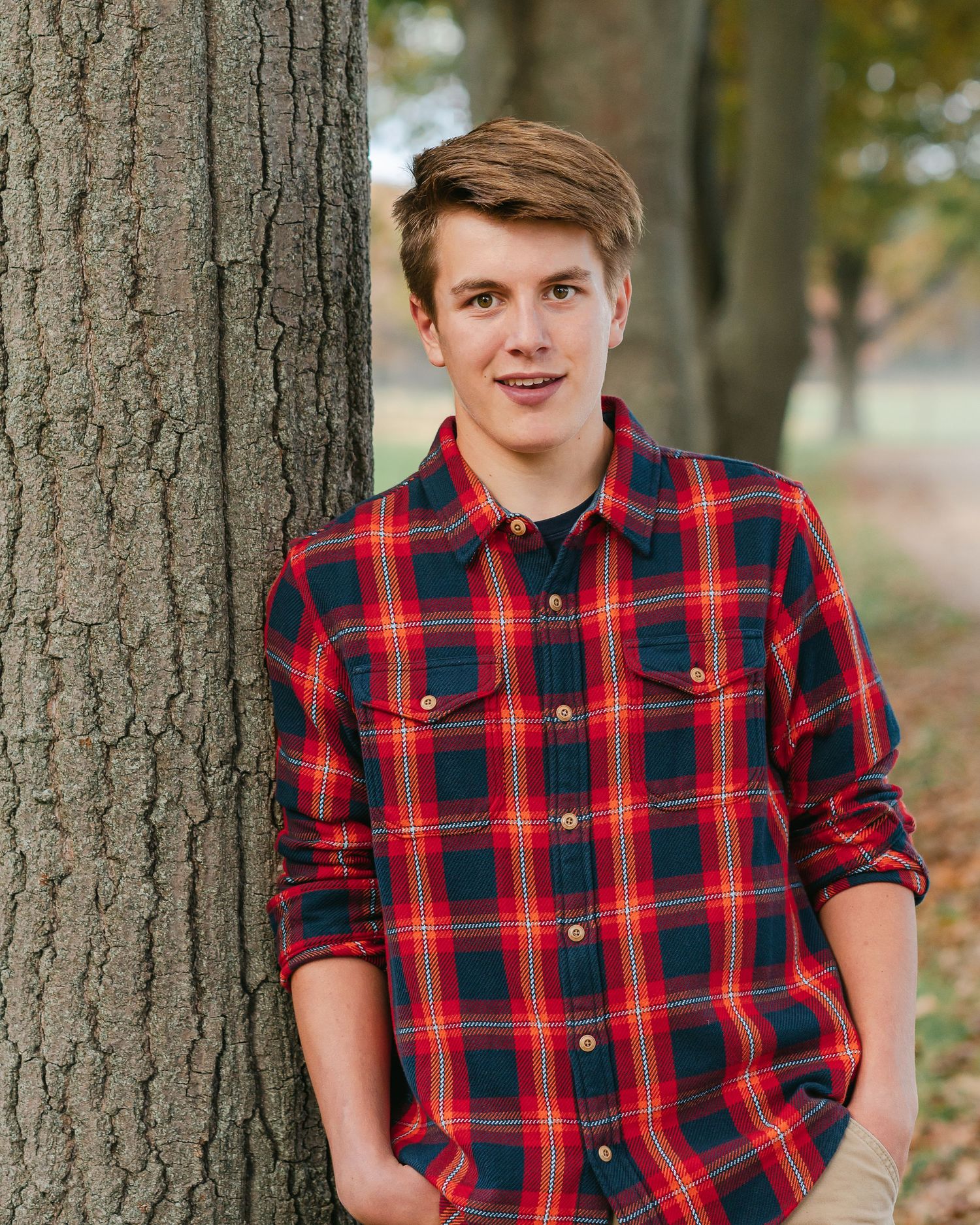 Casual portrait in red plaid shirt against tree trunk backdrop.