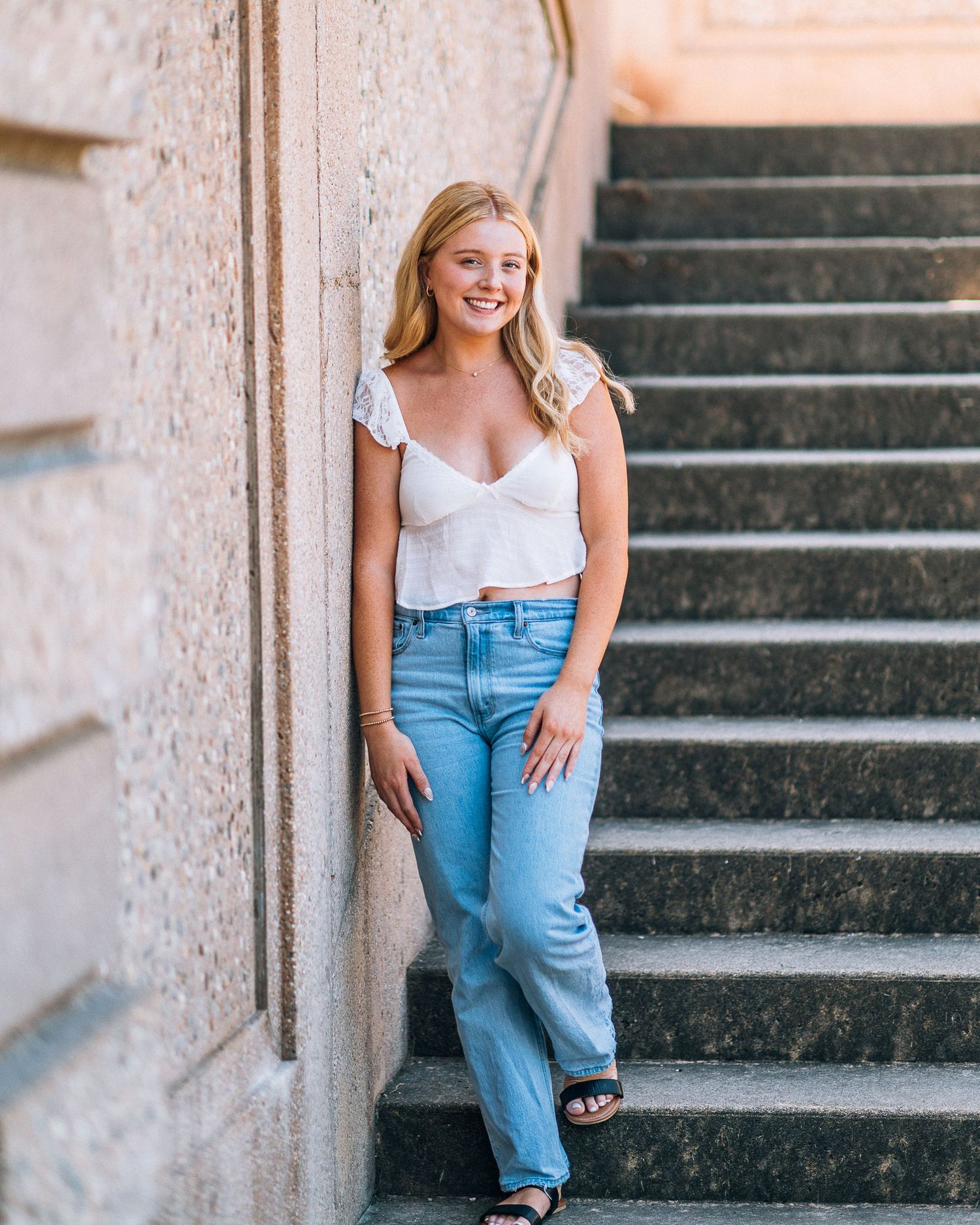 Casual portrait on stone steps wearing white top and blue jeans.