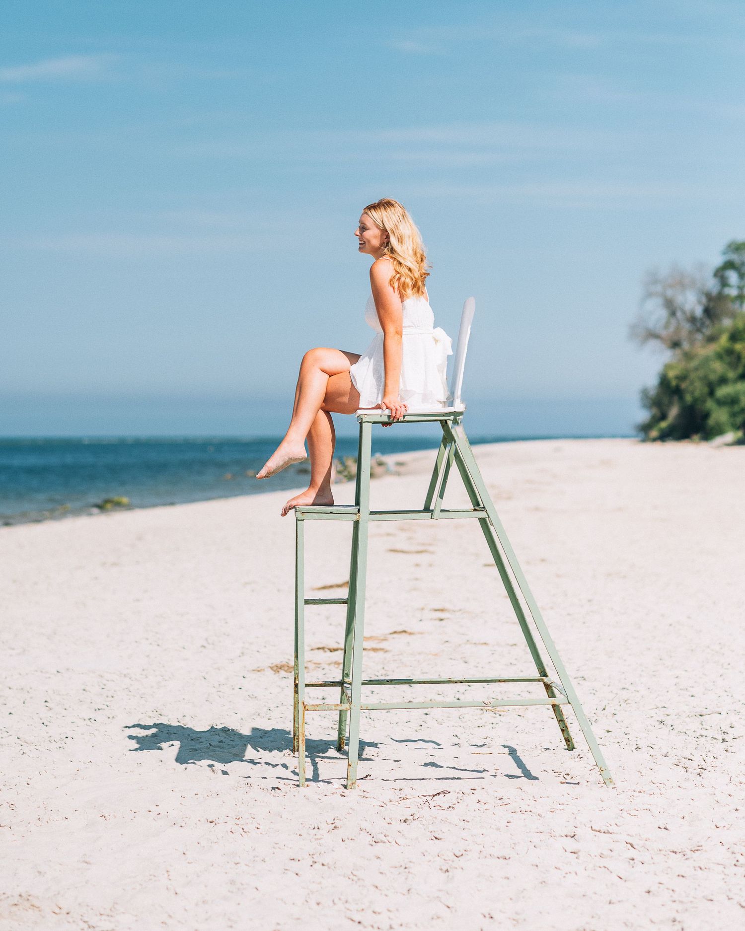 Person in white dress sitting on lifeguard chair at sunny beach.