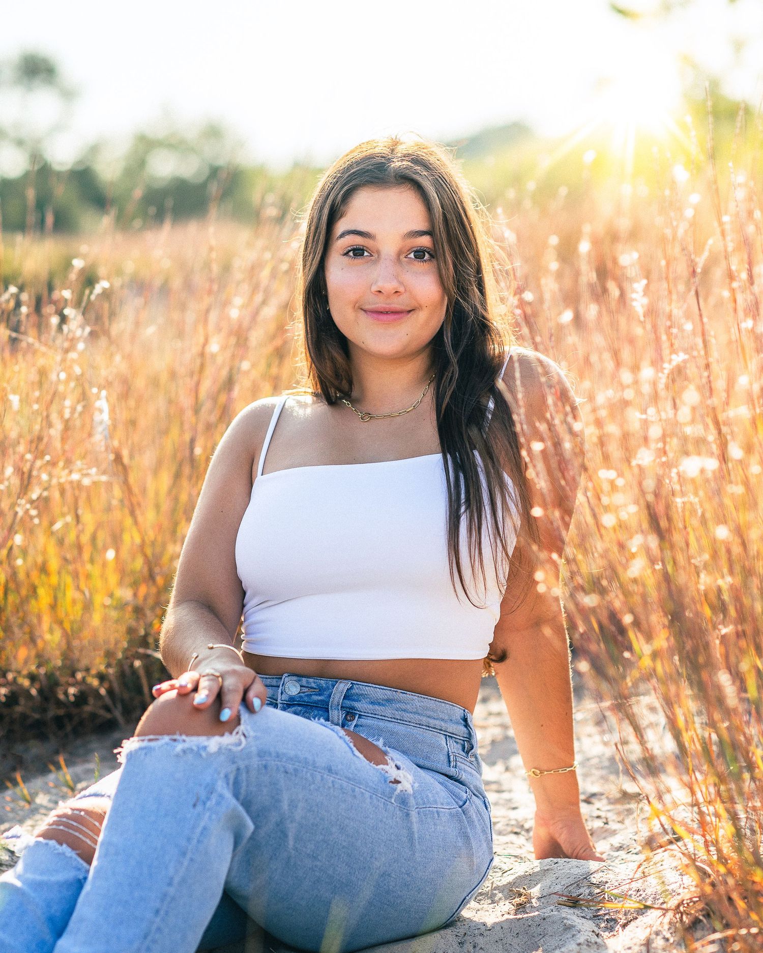 Summer portrait in white crop top and jeans with golden sunset in tall grass field.