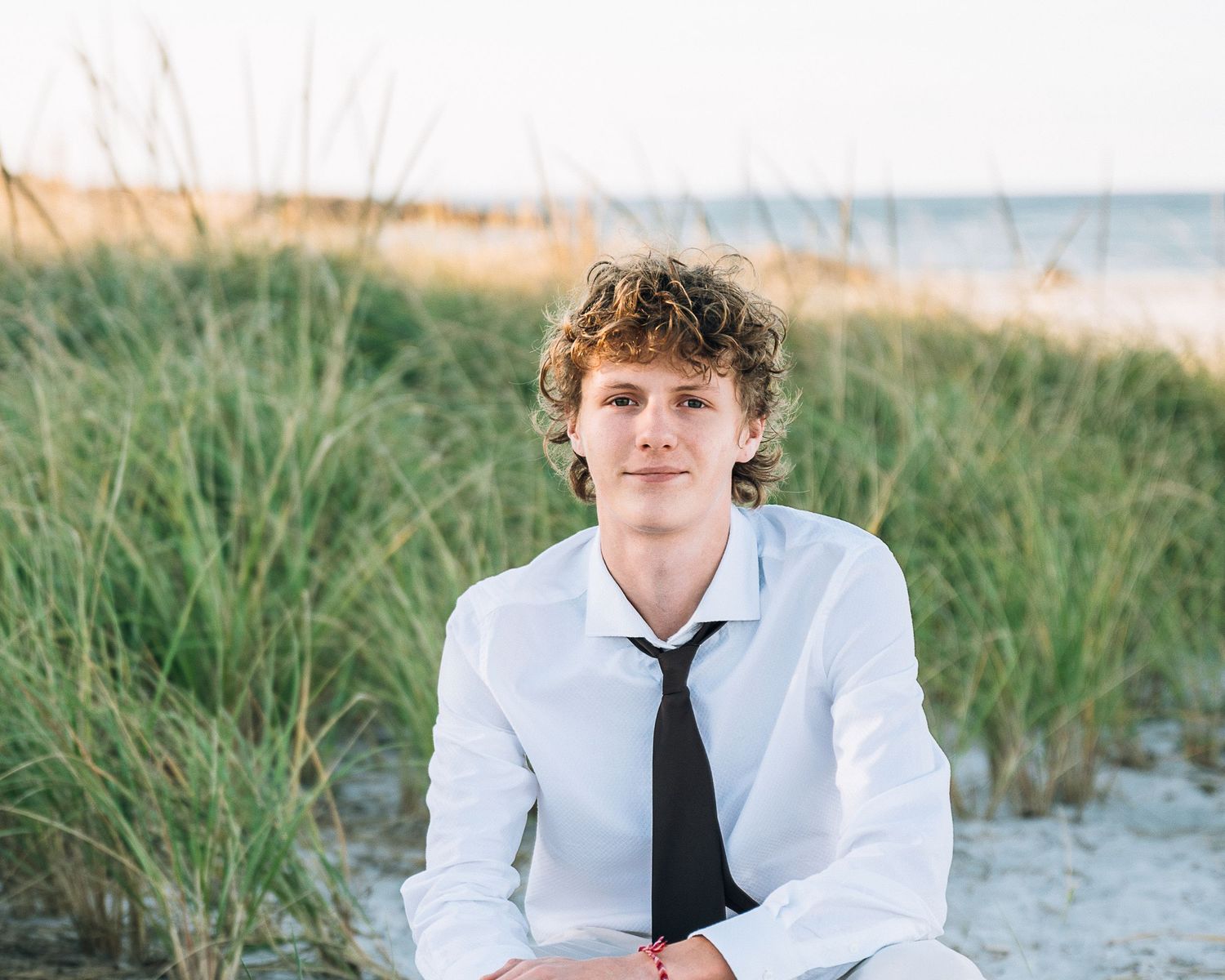 Professional portrait in white shirt and tie against beach grass and ocean background.