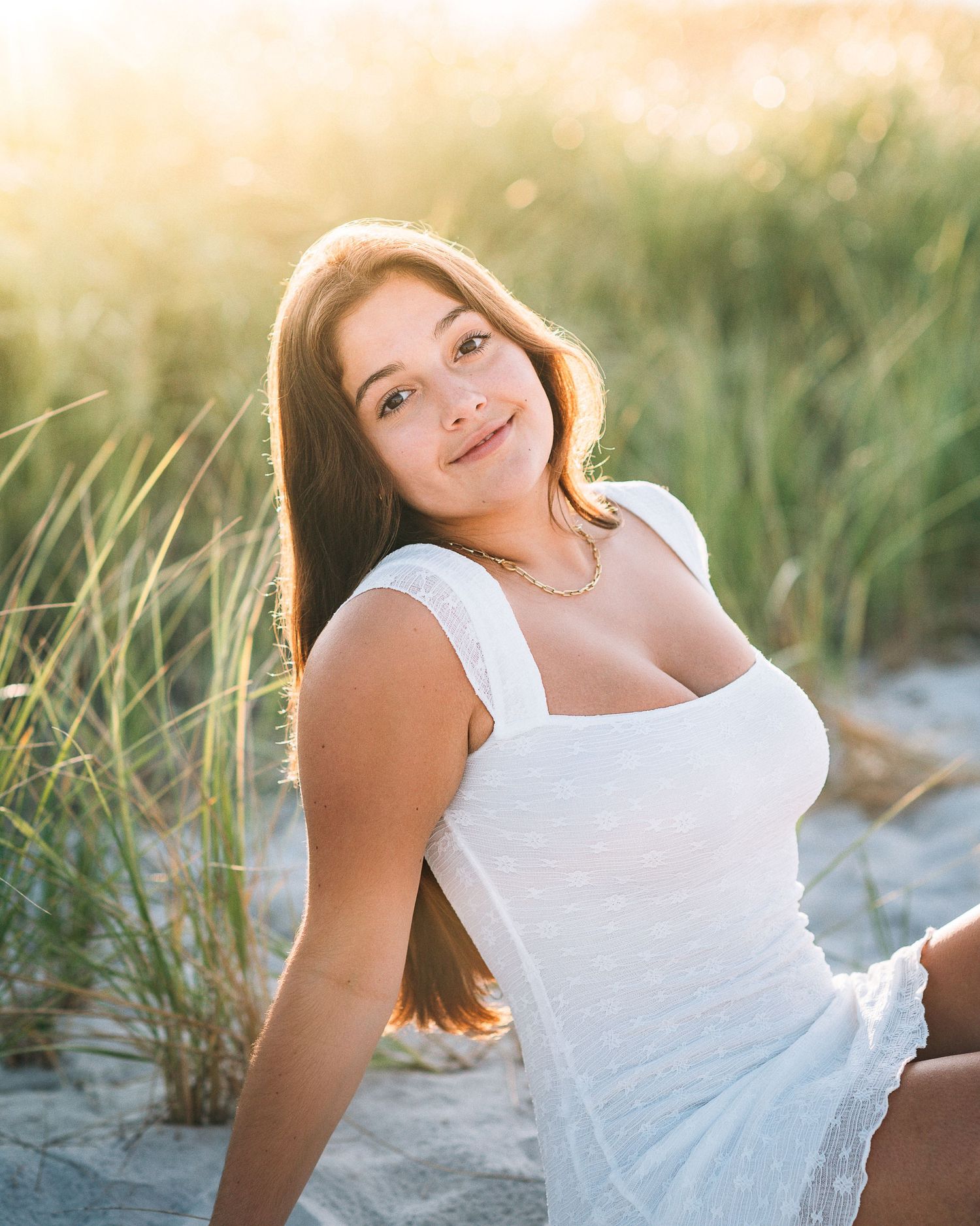 White sundress portrait at beach with warm sunset glow through tall grass.