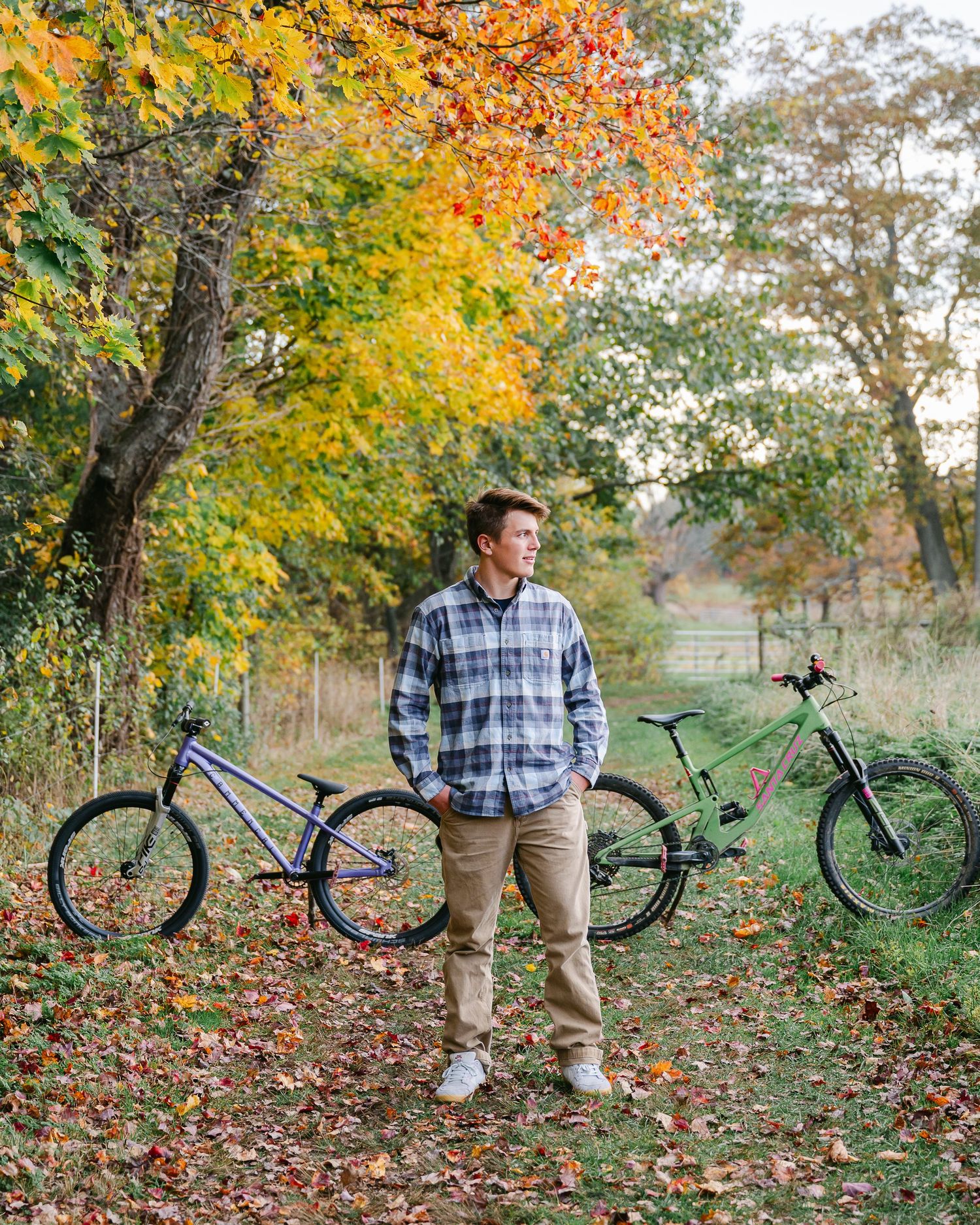 Person standing with mountain bikes among fall foliage.