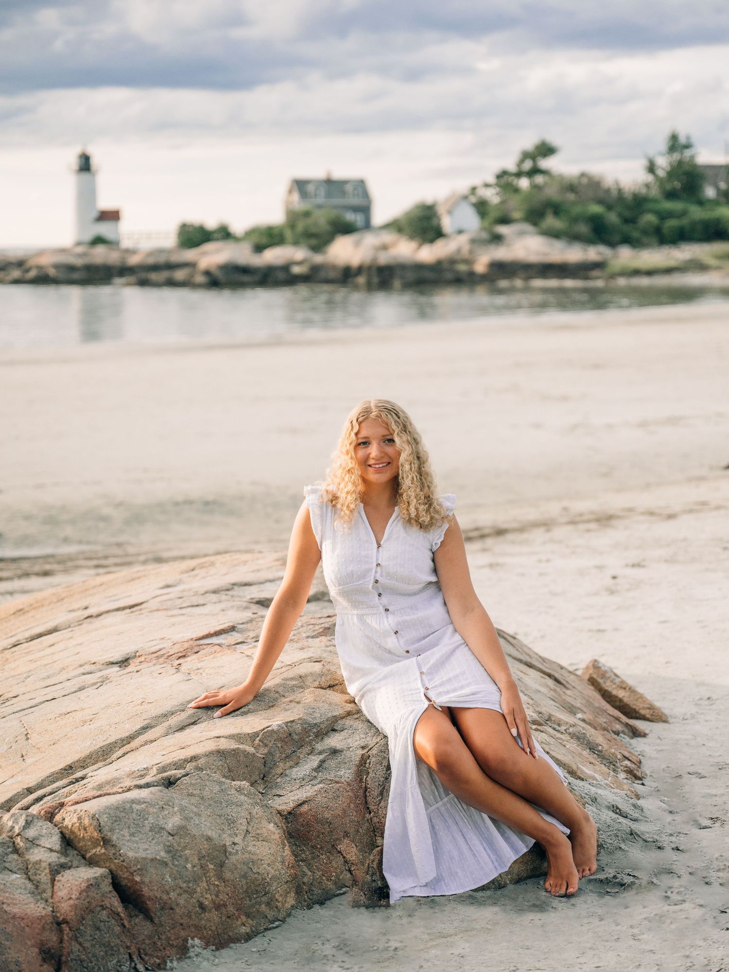 White dress on rocky coastline with lighthouse and buildings visible in distant background.