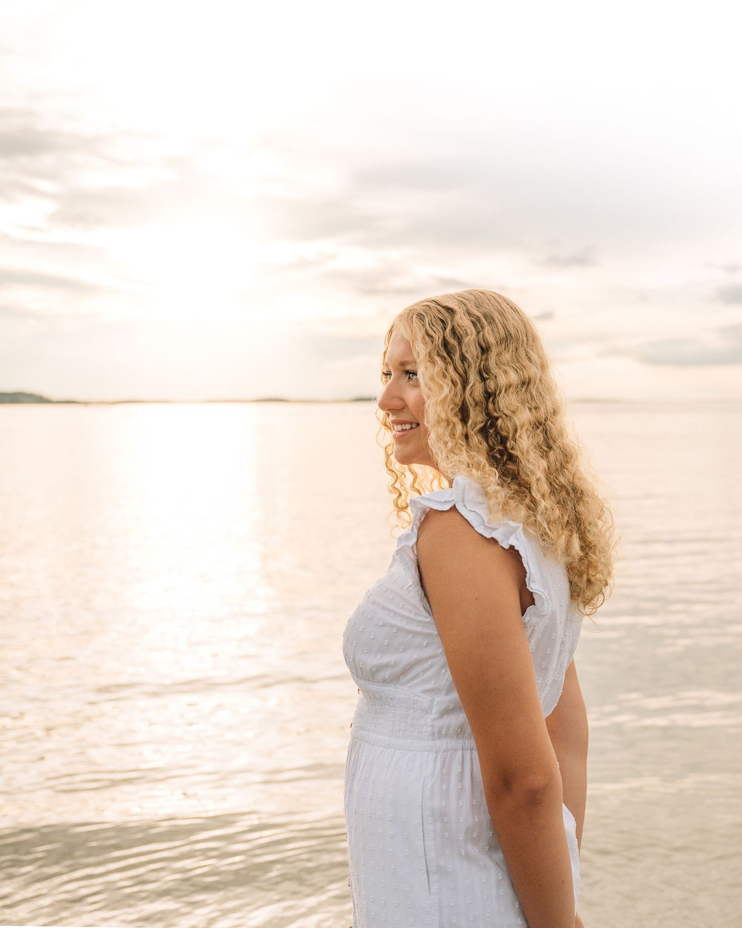Side profile at sunset wearing white dress against golden ocean backdrop.