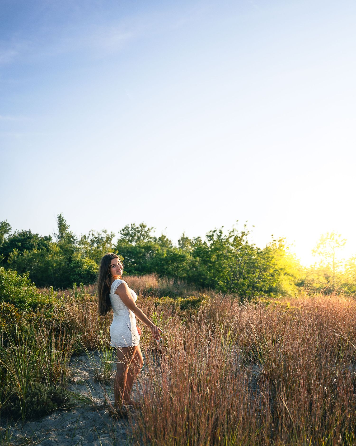 Woman in white dress stands in golden field at sunset.
