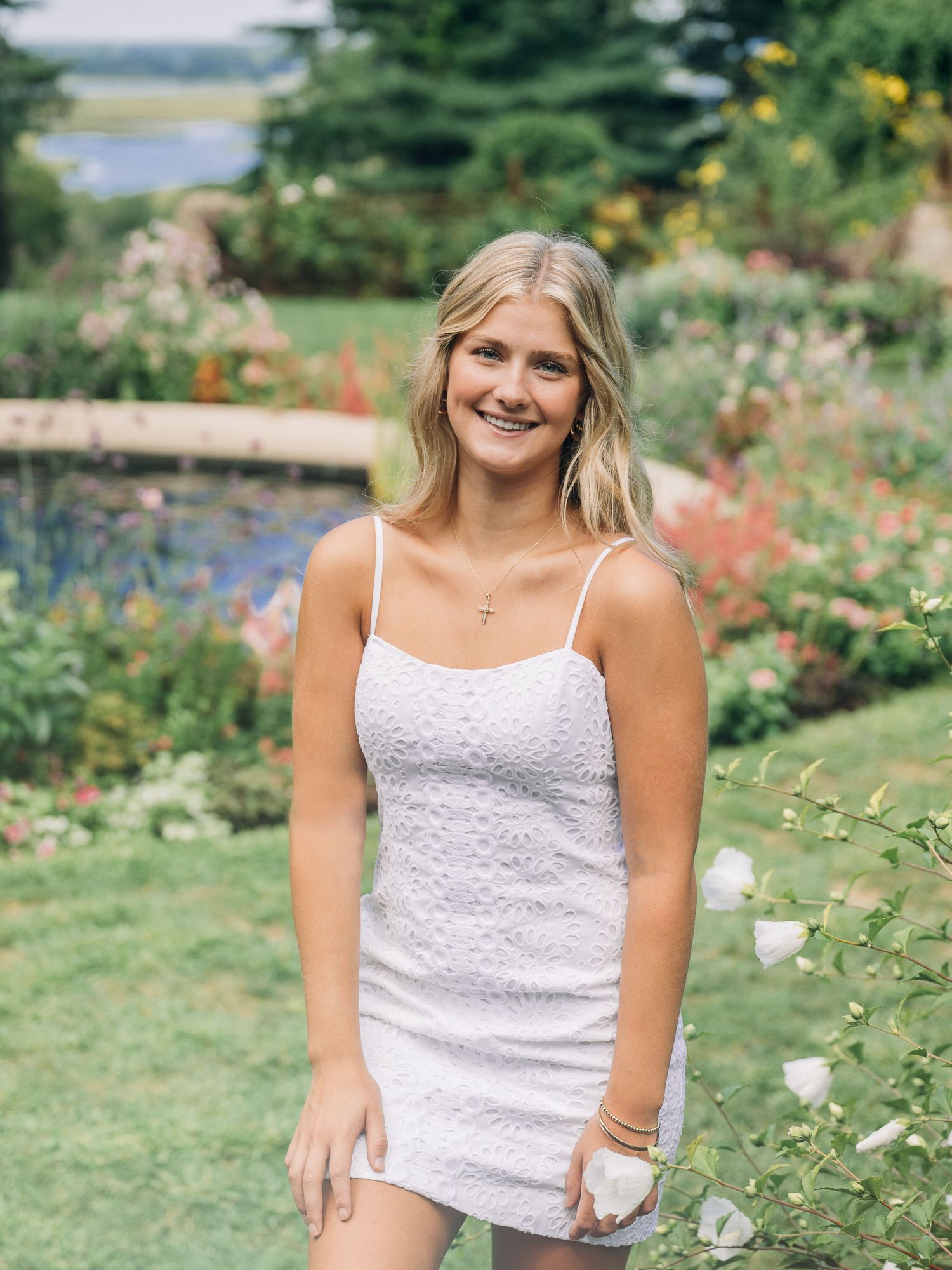 White eyelet dress worn in a vibrant summer garden with colorful flowers and water feature.