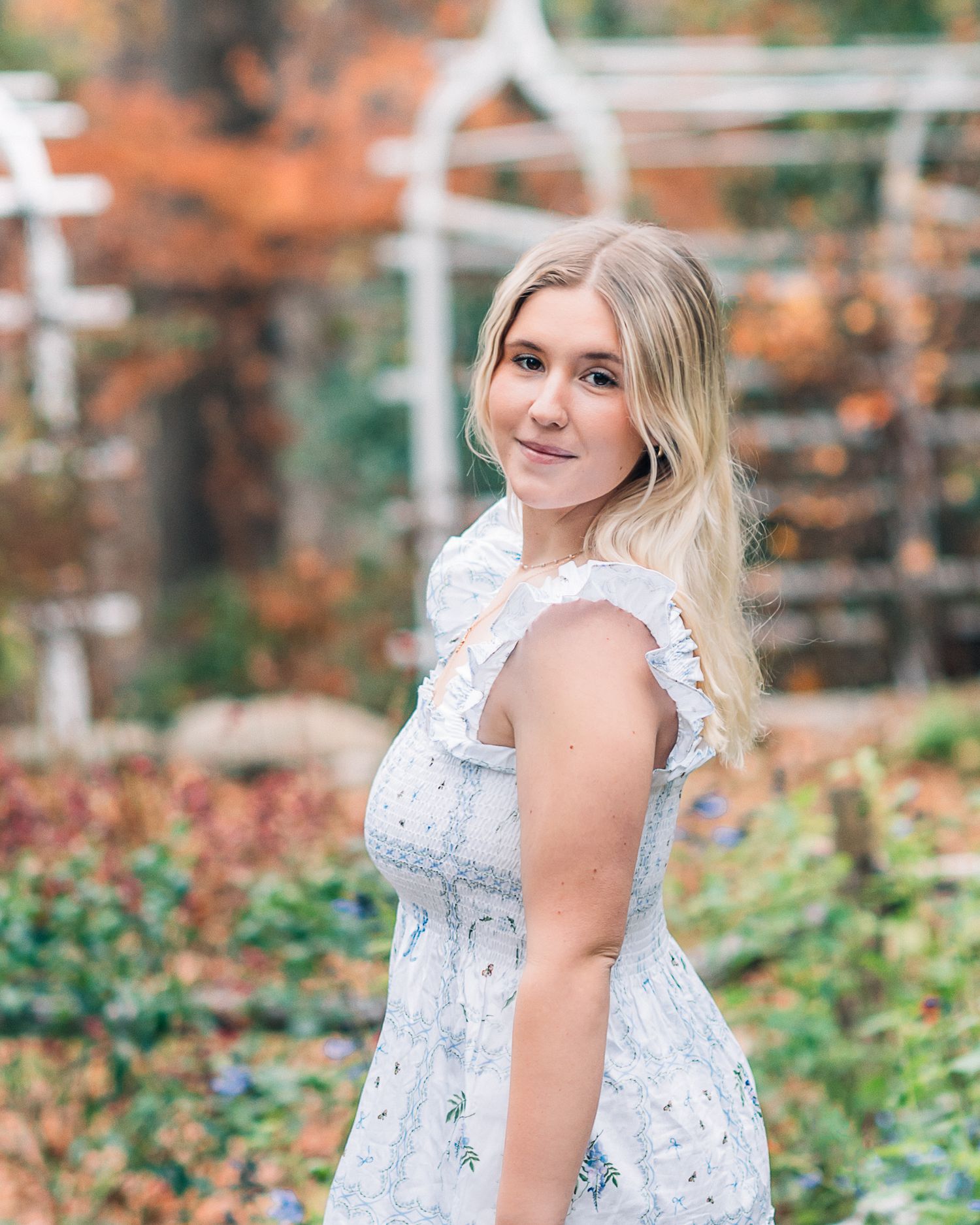 Portrait in white lace dress standing in garden with autumn foliage.