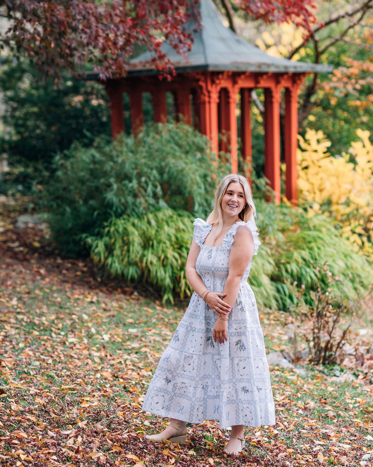 White dress portrait near red pagoda structure in autumn garden setting.
