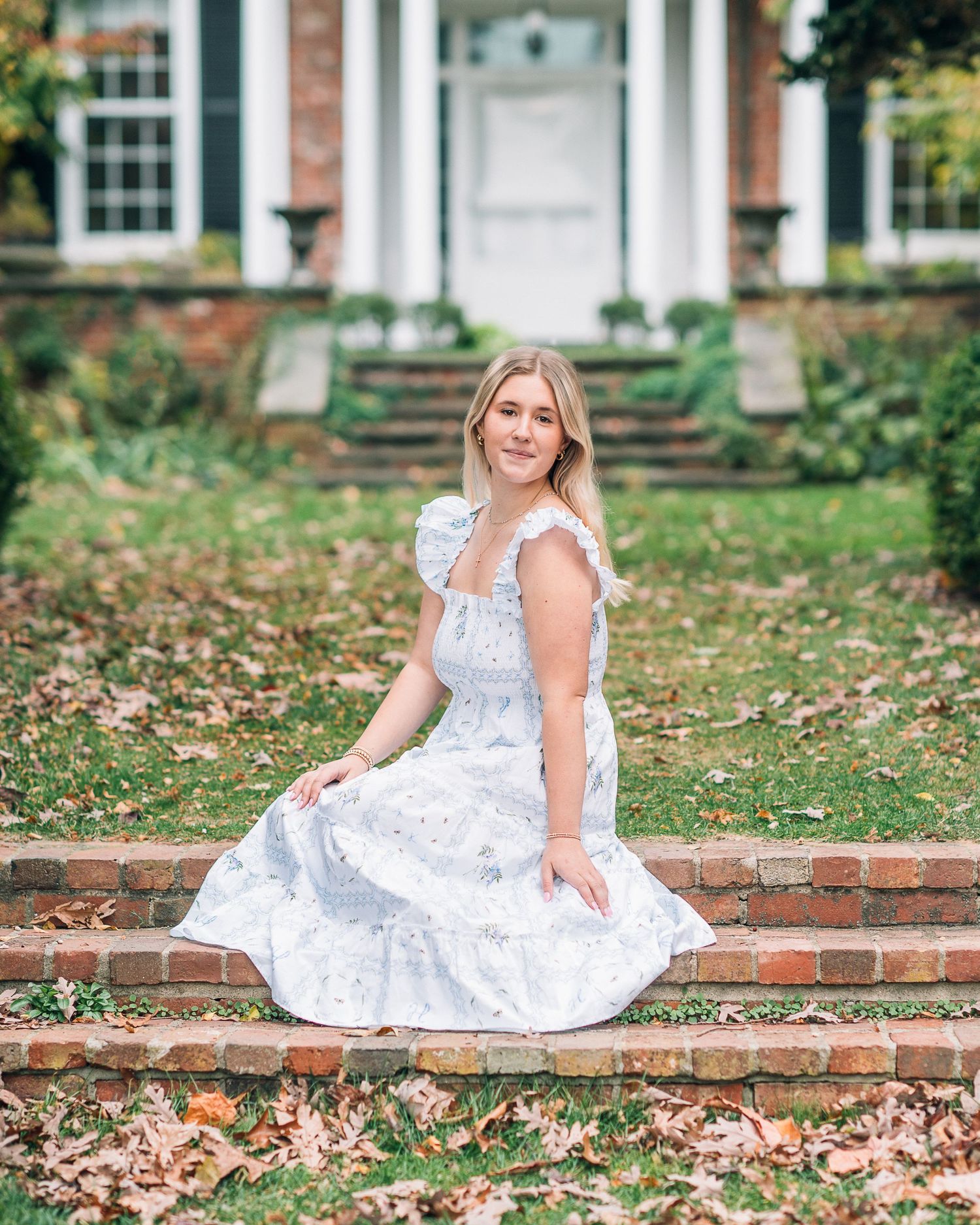 Portrait on brick steps in white lace dress with colonial style architecture background.