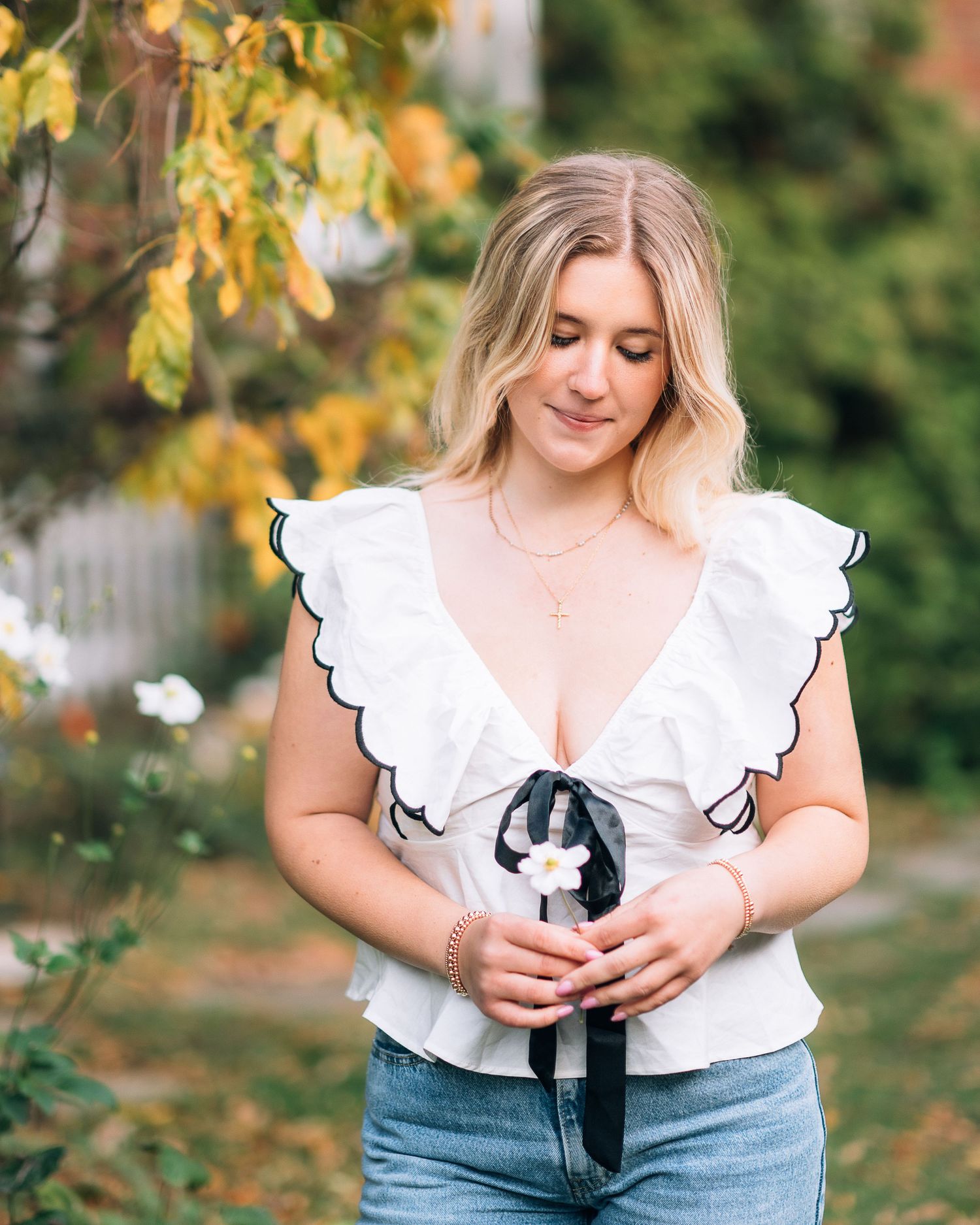 Portrait in white ruffled top with black bow detail against autumn foliage.