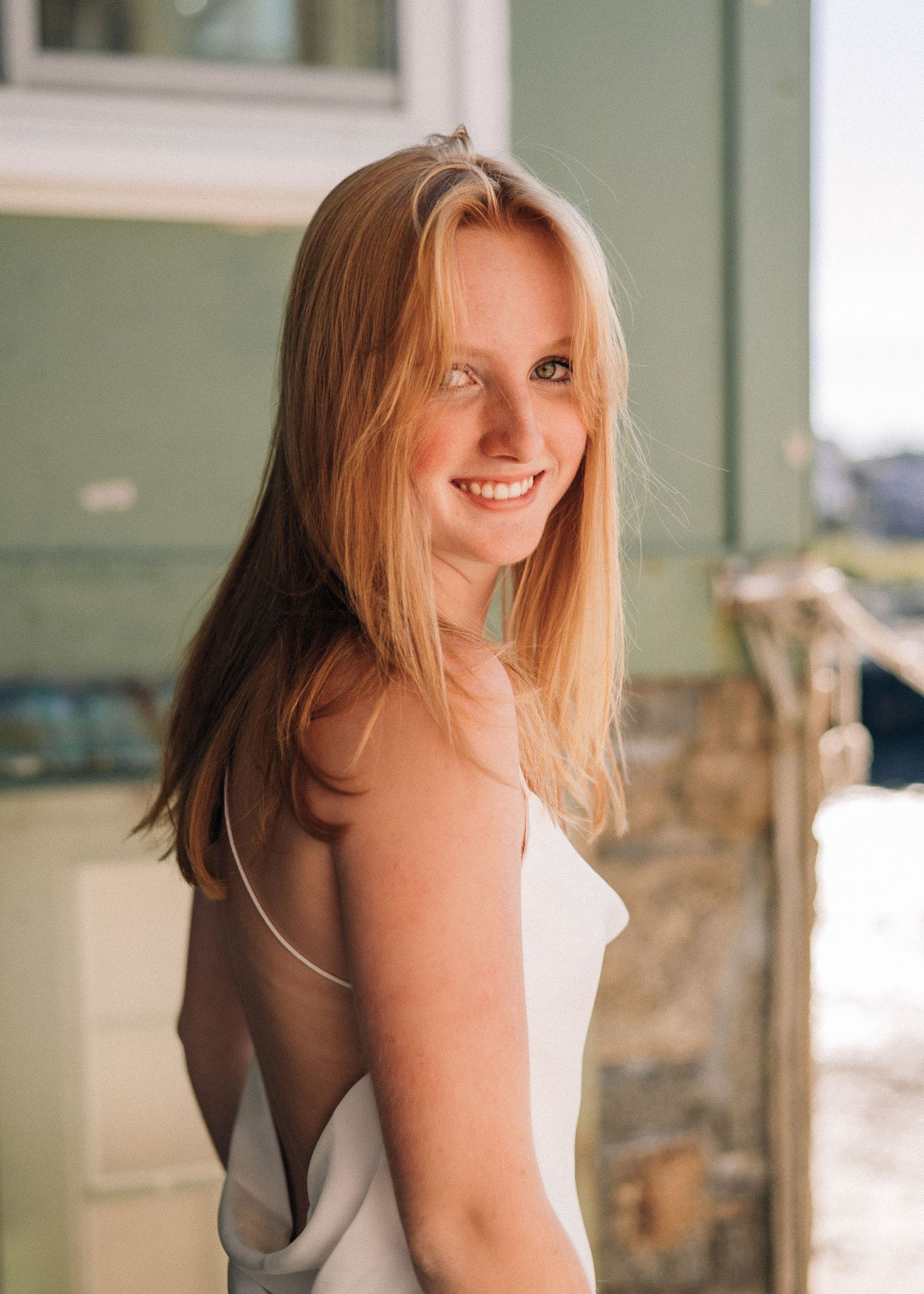 Portrait of someone with long blonde hair in backless dress against green wall.