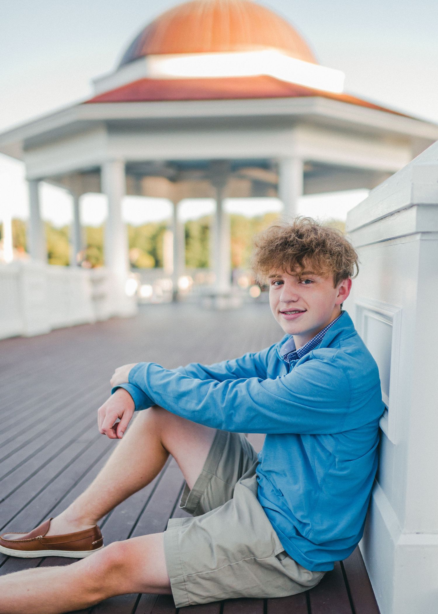 A person in a blue jacket sits casually on a wooden deck near a gazebo.