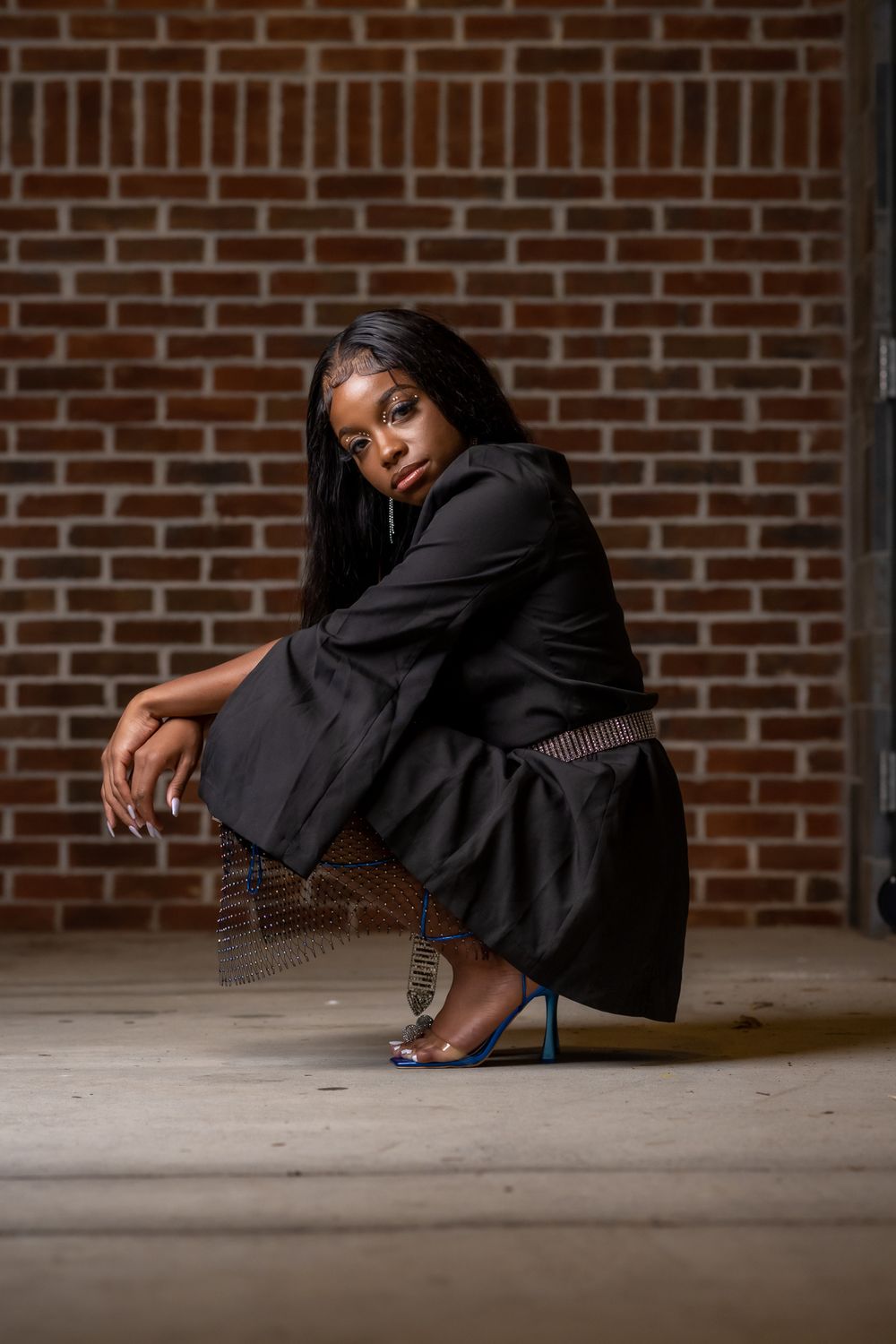 Artistic portrait showing person in black outfit against brick wall in dramatic lighting.