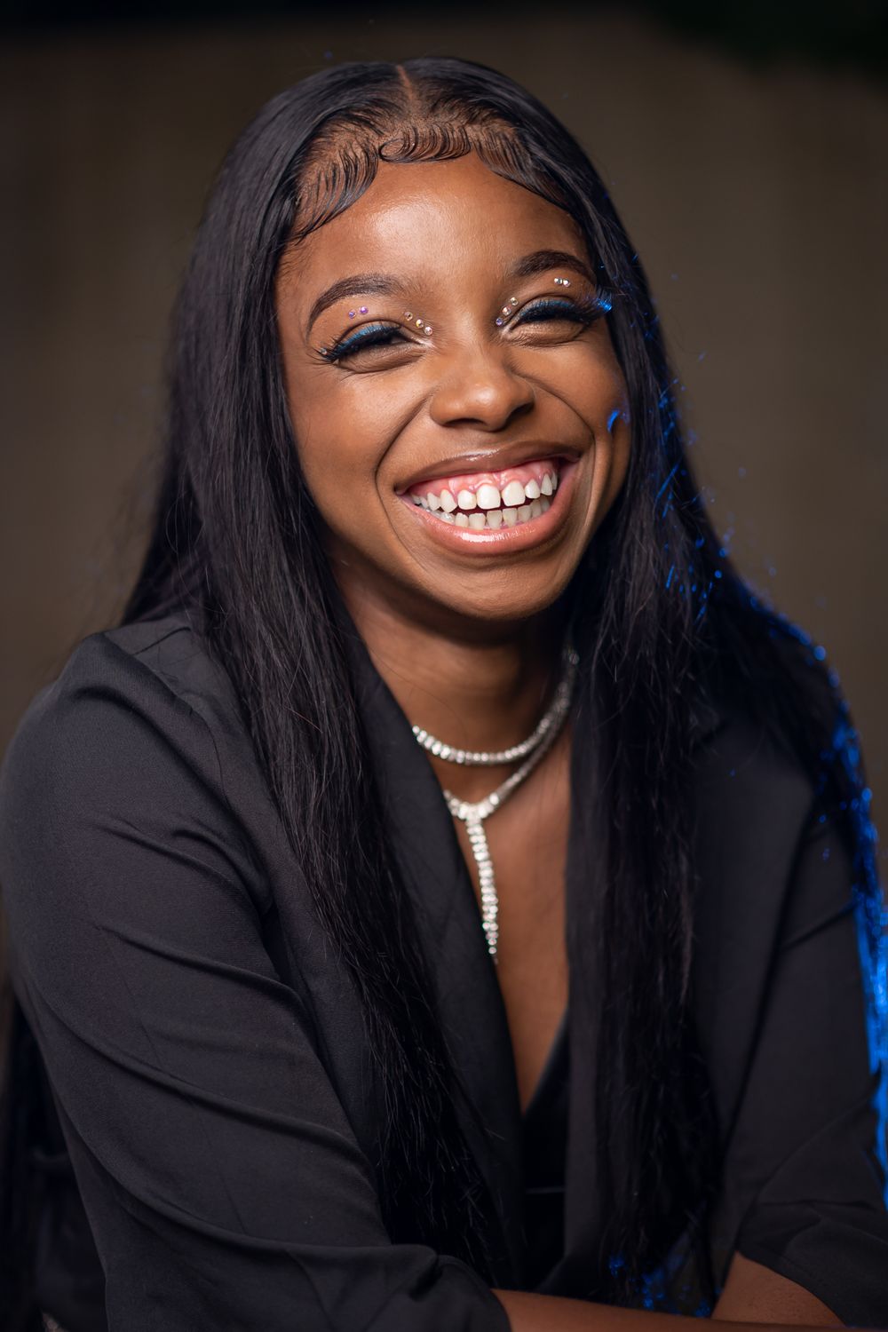 Studio portrait against dark background with elegant black attire and pearl necklace.
