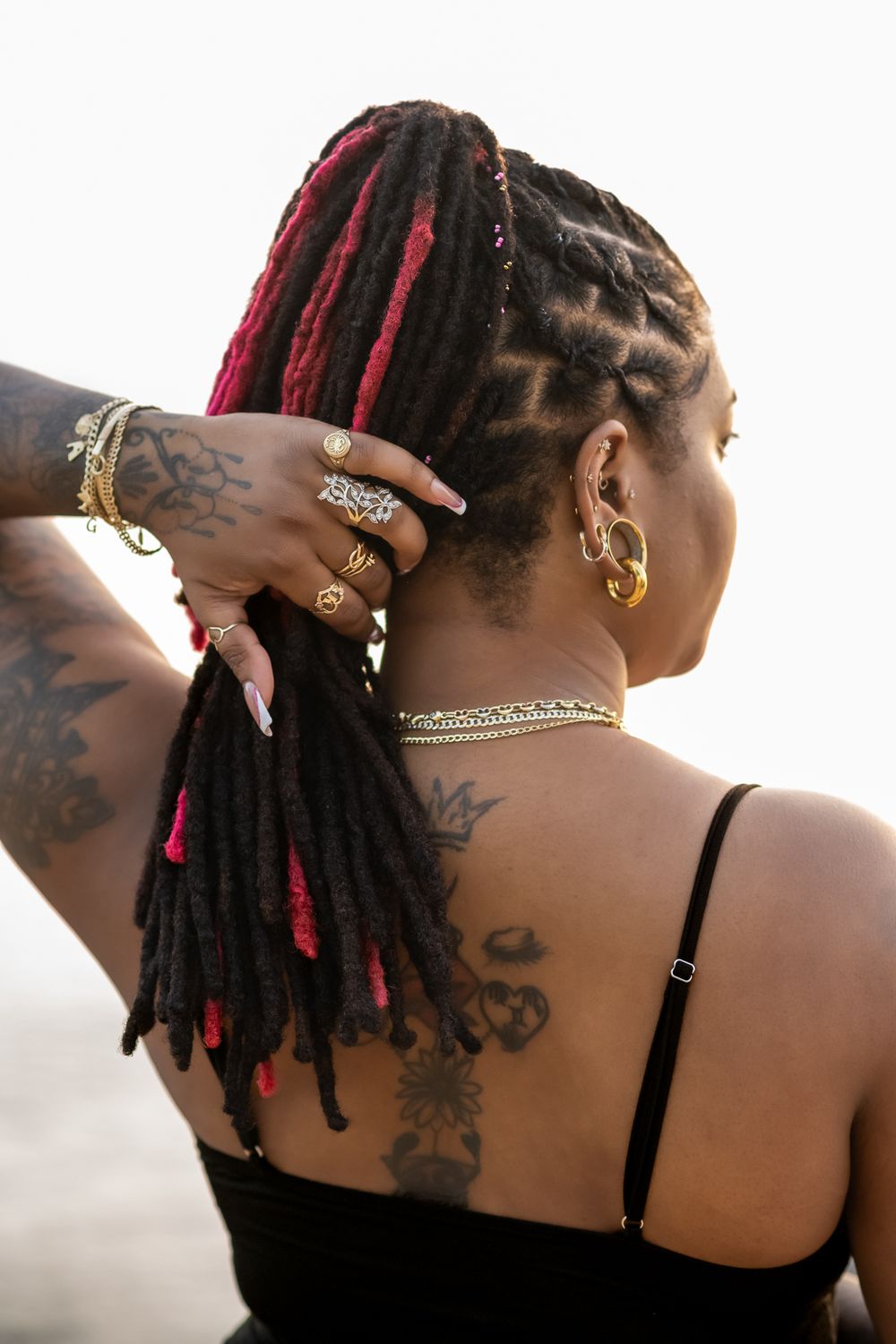 Close-up of decorated dreadlocks with red highlights and gold jewelry against white background.