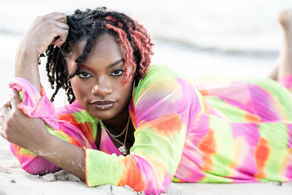 Person wearing vibrant tie-dye outfit lounging on beach sand.